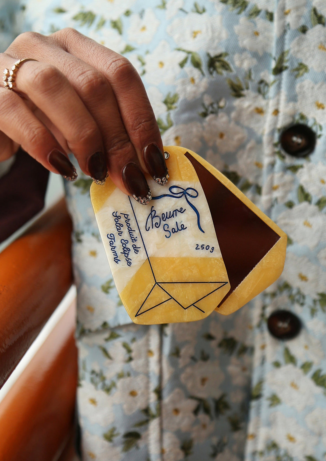 Hand holding a butter shaped compact mirror, against a floral-patterned background.