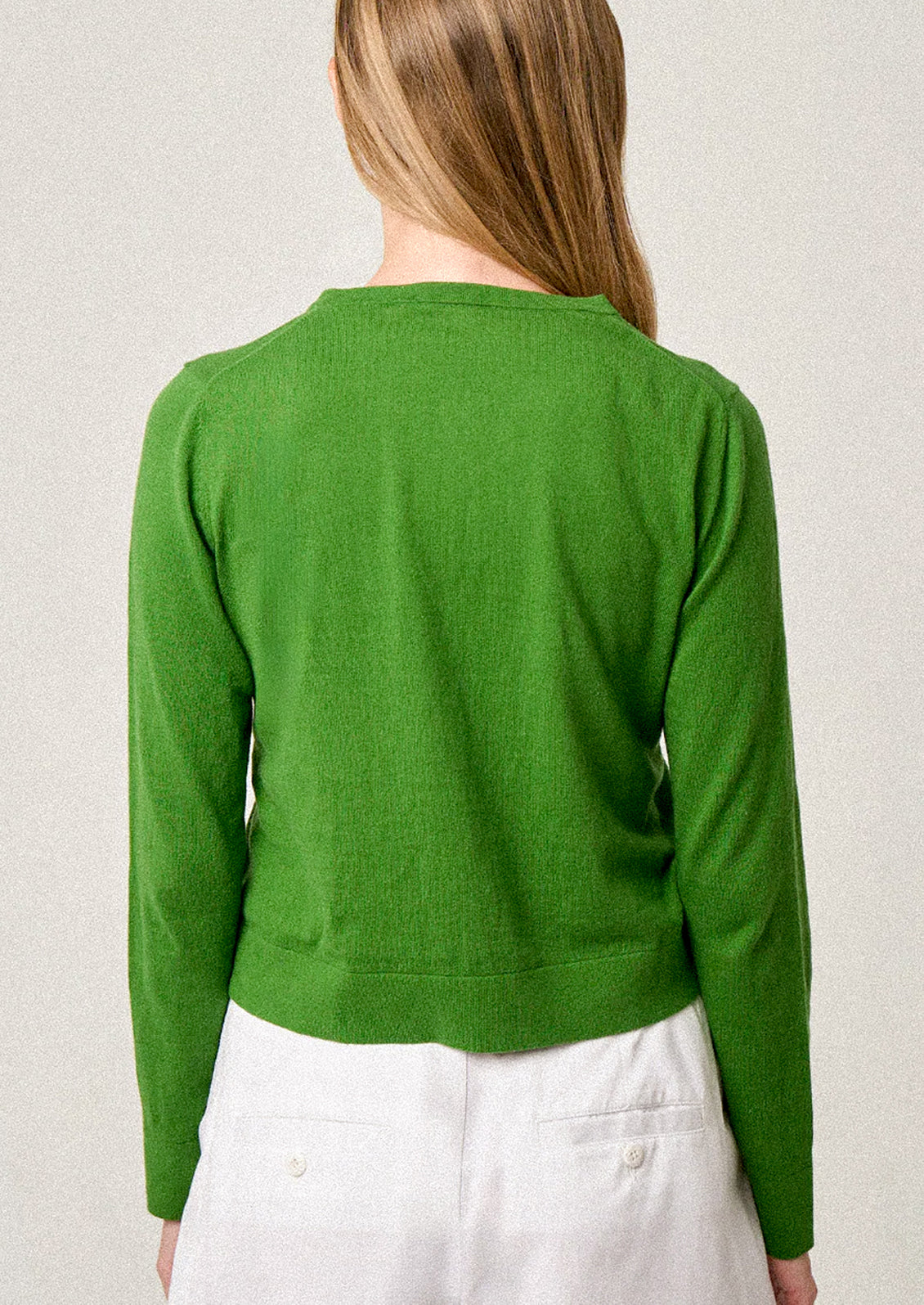 Person wearing a green cardigan over a white outfit on a plain background