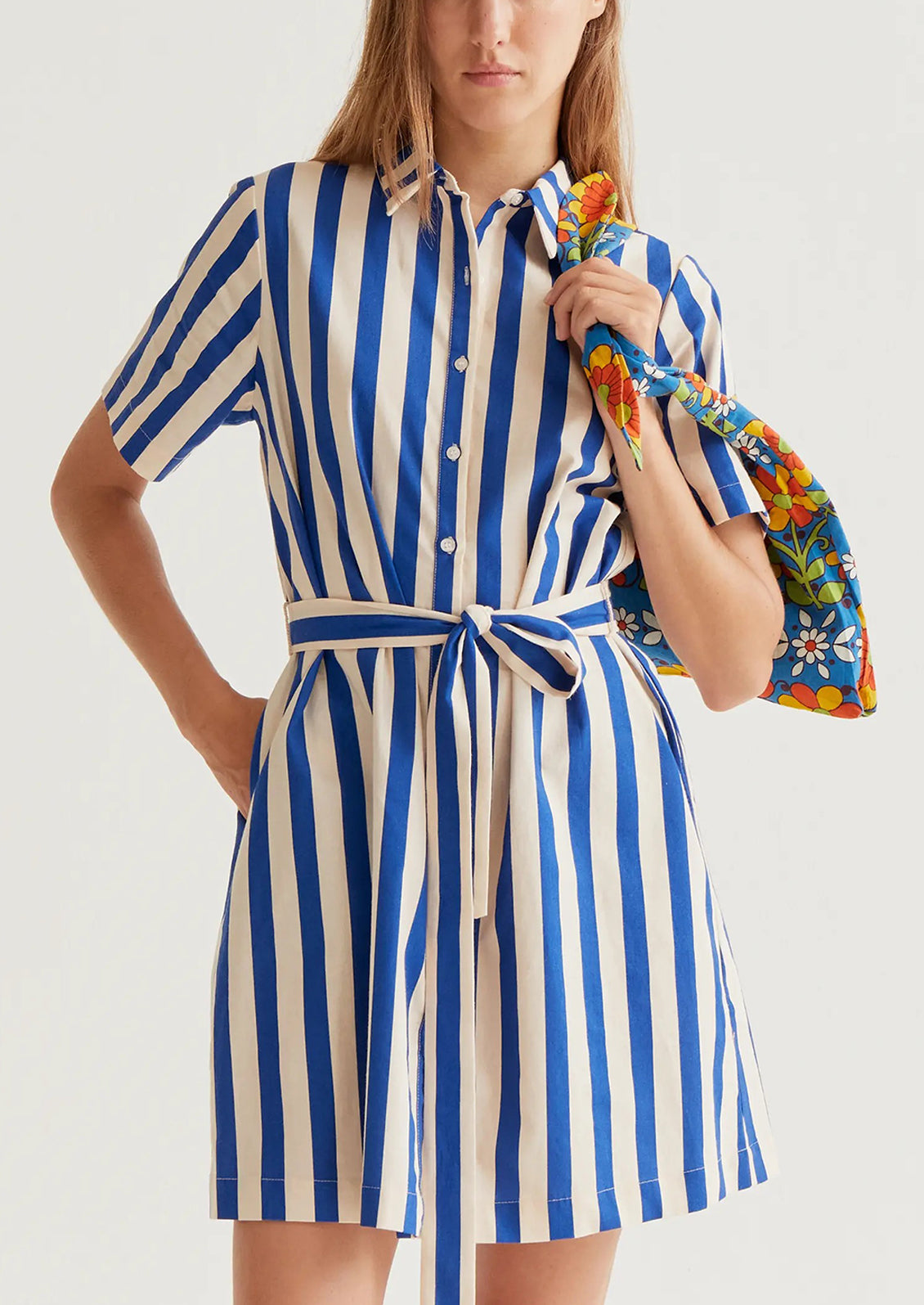 Woman wearing a blue and white striped dress holding a colorful jacket.