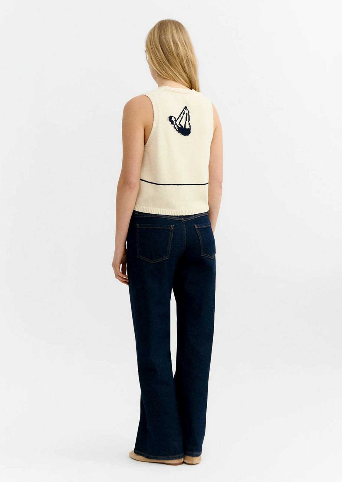 Woman wearing a sleeveless top and dark jeans against a white background