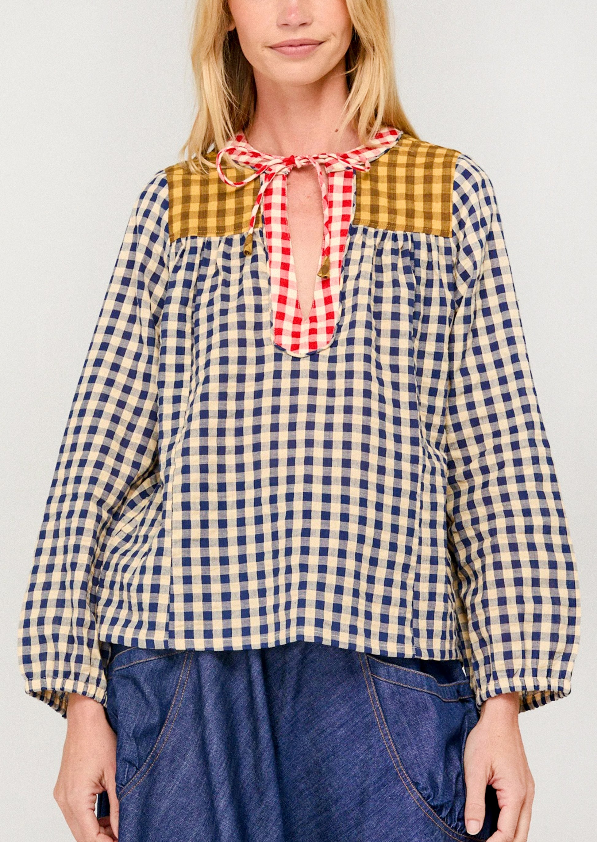 Woman wearing a checkered blouse with a red and white plaid bow tie against a plain background