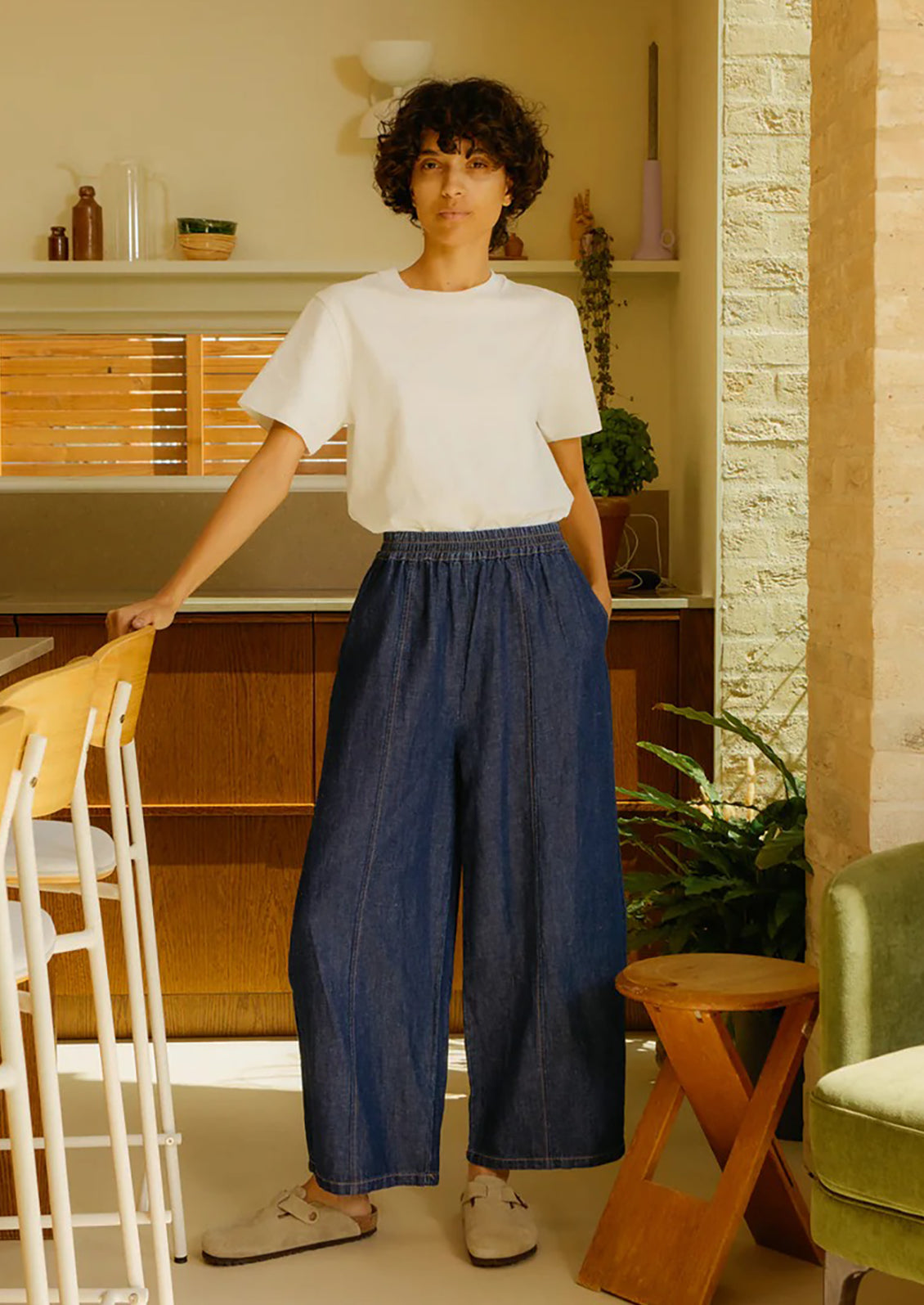 Person standing in a kitchen wearing a white top and blue pants.