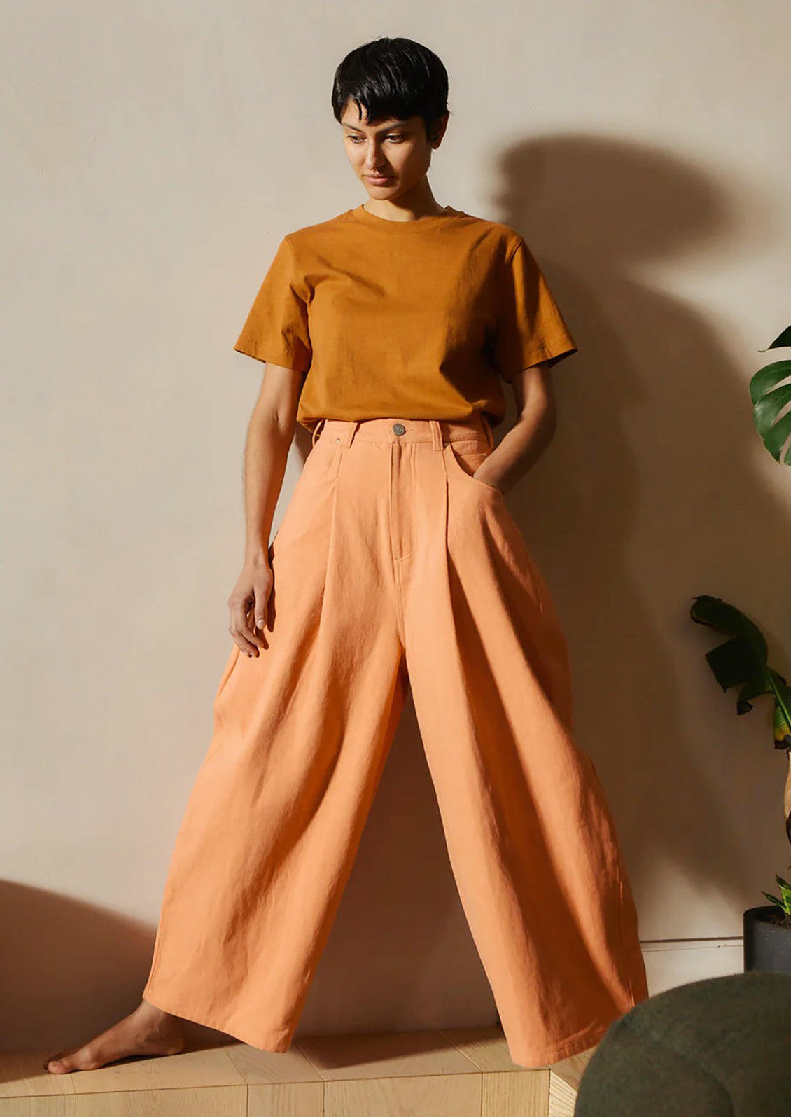 Person wearing a mustard yellow top and peach pants against a neutral wall.