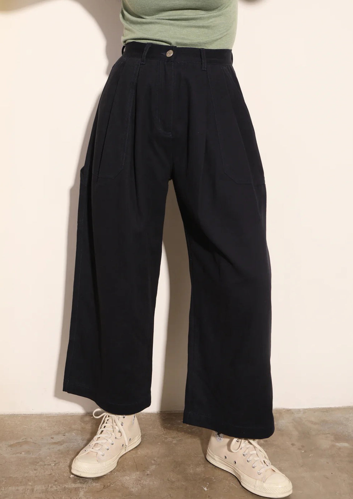 Person wearing navy wide-leg pants and white sneakers against a plain background