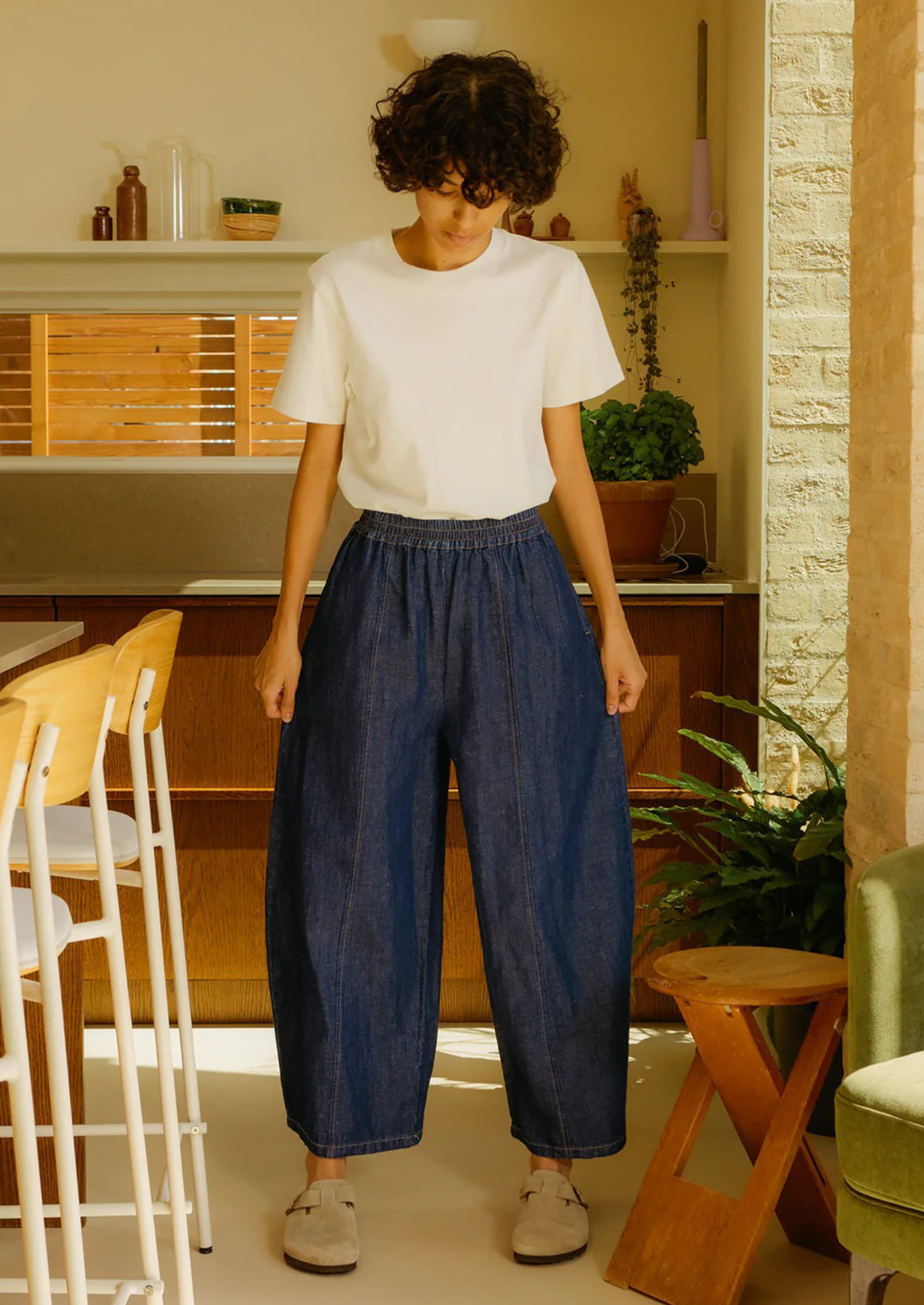 Person wearing a white shirt and blue pants standing in a kitchen.