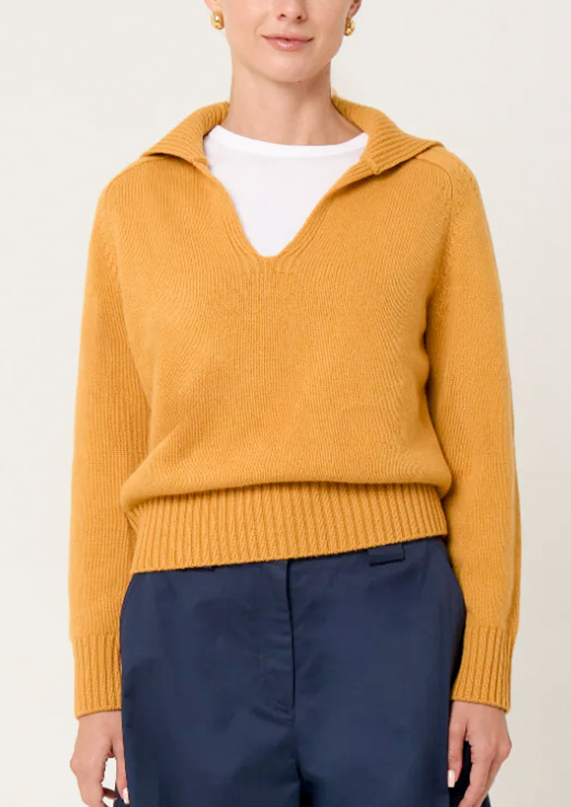 Person wearing a mustard yellow sweater with a white shirt underneath on a plain background