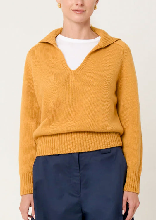 Person wearing a mustard yellow sweater with a white shirt underneath on a plain background