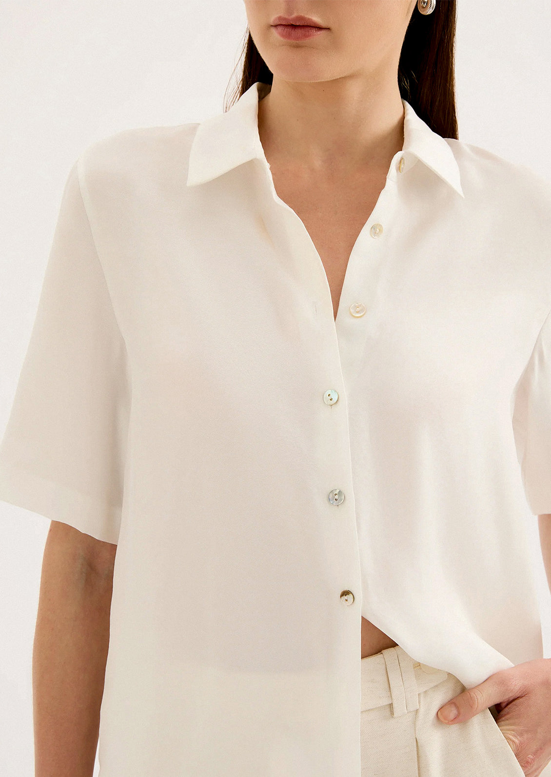 A woman wearing a draped short sleeve button up shirt in white.