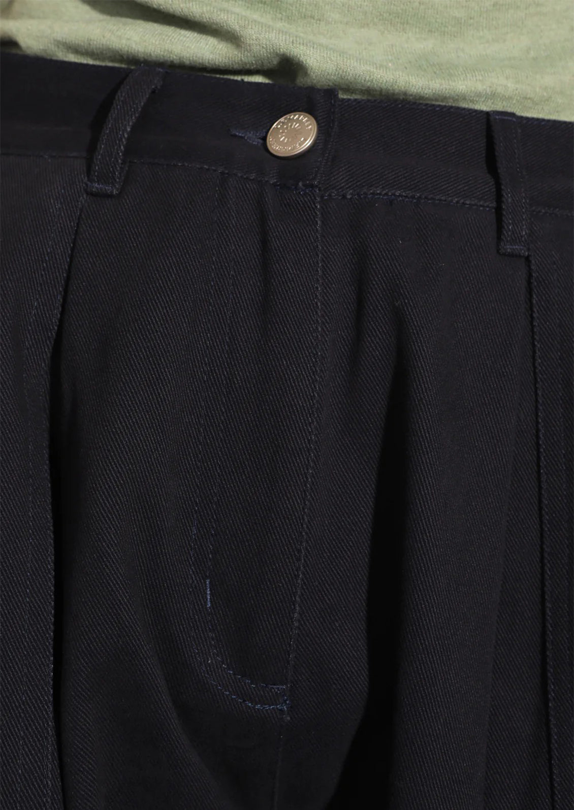 Close-up of black pants with a button and green shirt in the background
