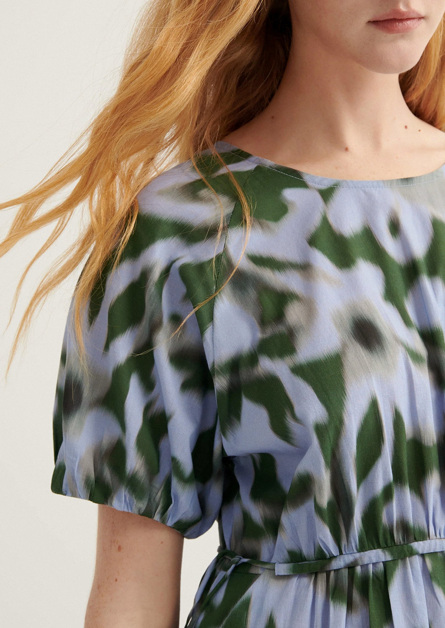 Close-up of a person wearing a floral dress with green, white, and blue pattern.