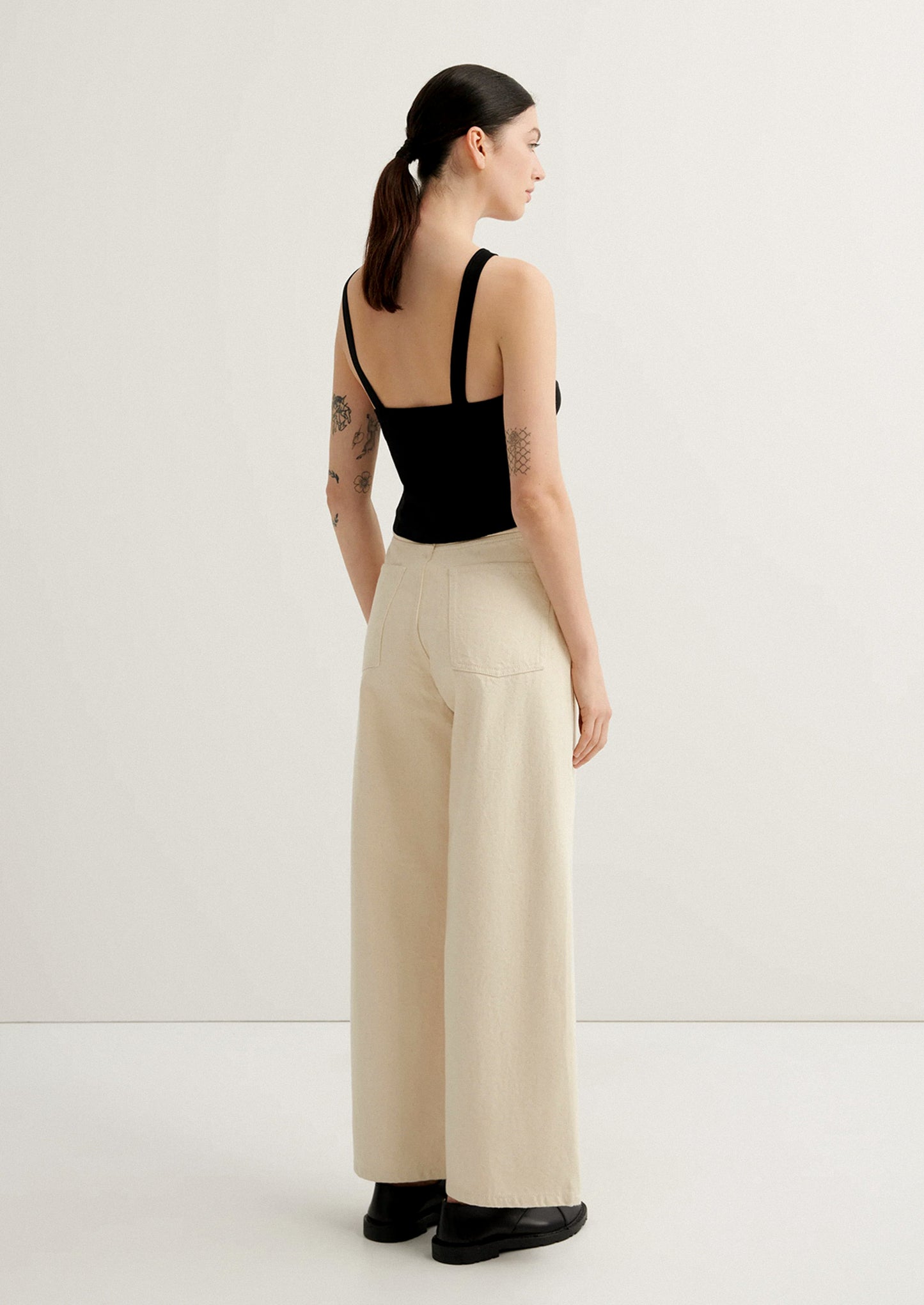 Woman wearing a black top and beige wide-leg pants on a white background