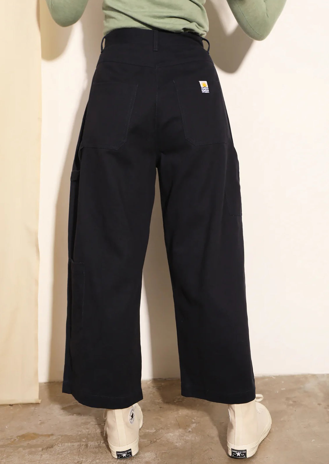 Person wearing black wide-leg pants with a visible brand logo against a plain background