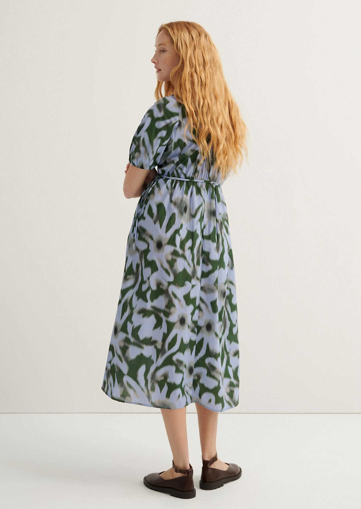 Woman wearing a patterned dress standing against a white background