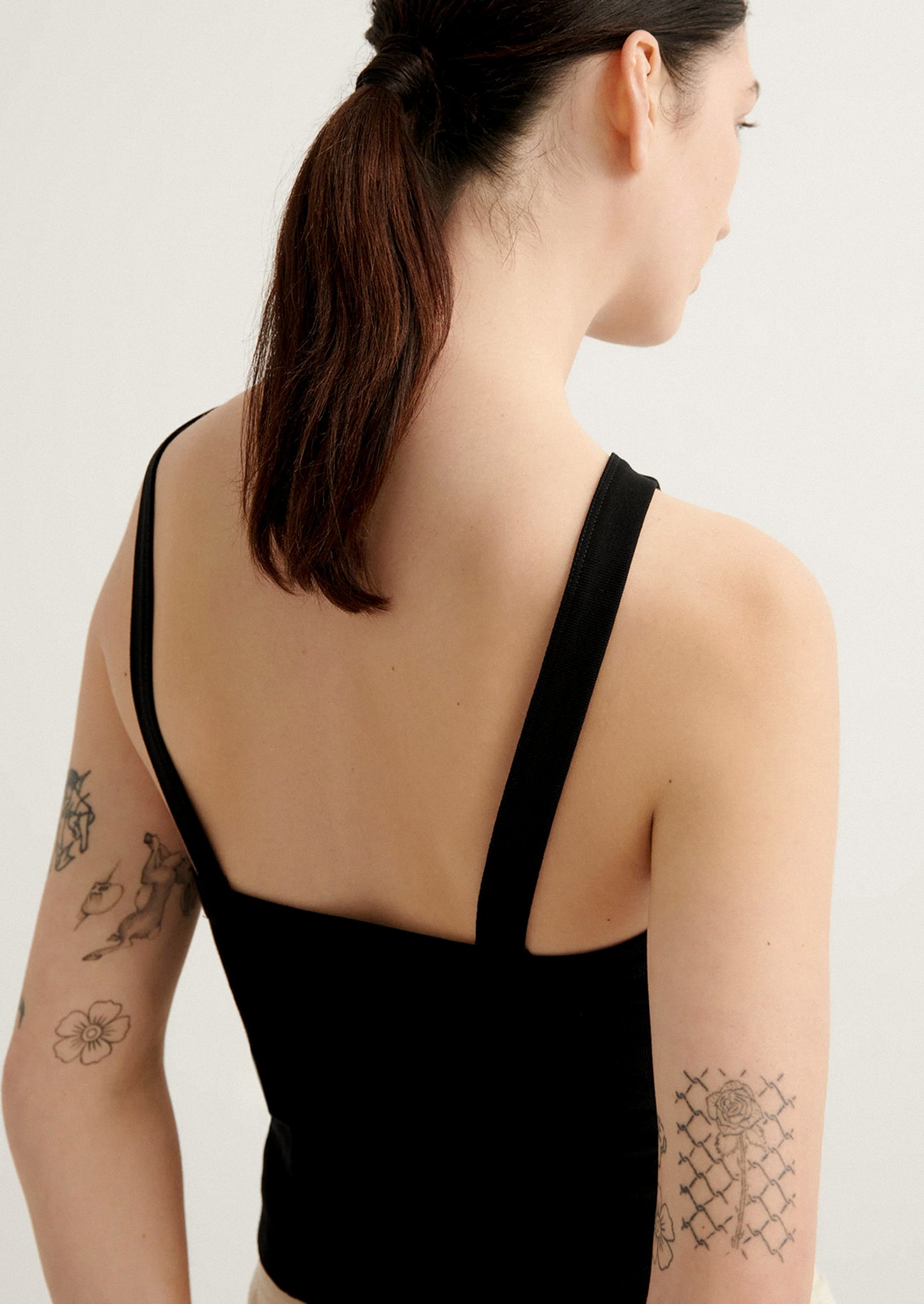 Person wearing a black sleeveless top with visible tattoos on arms, on a plain background