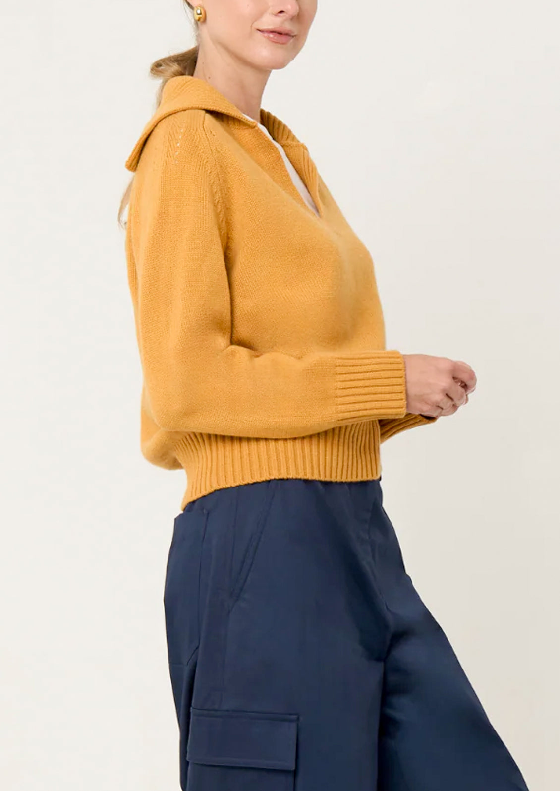 Person wearing a mustard yellow sweater and navy pants on a light gray background