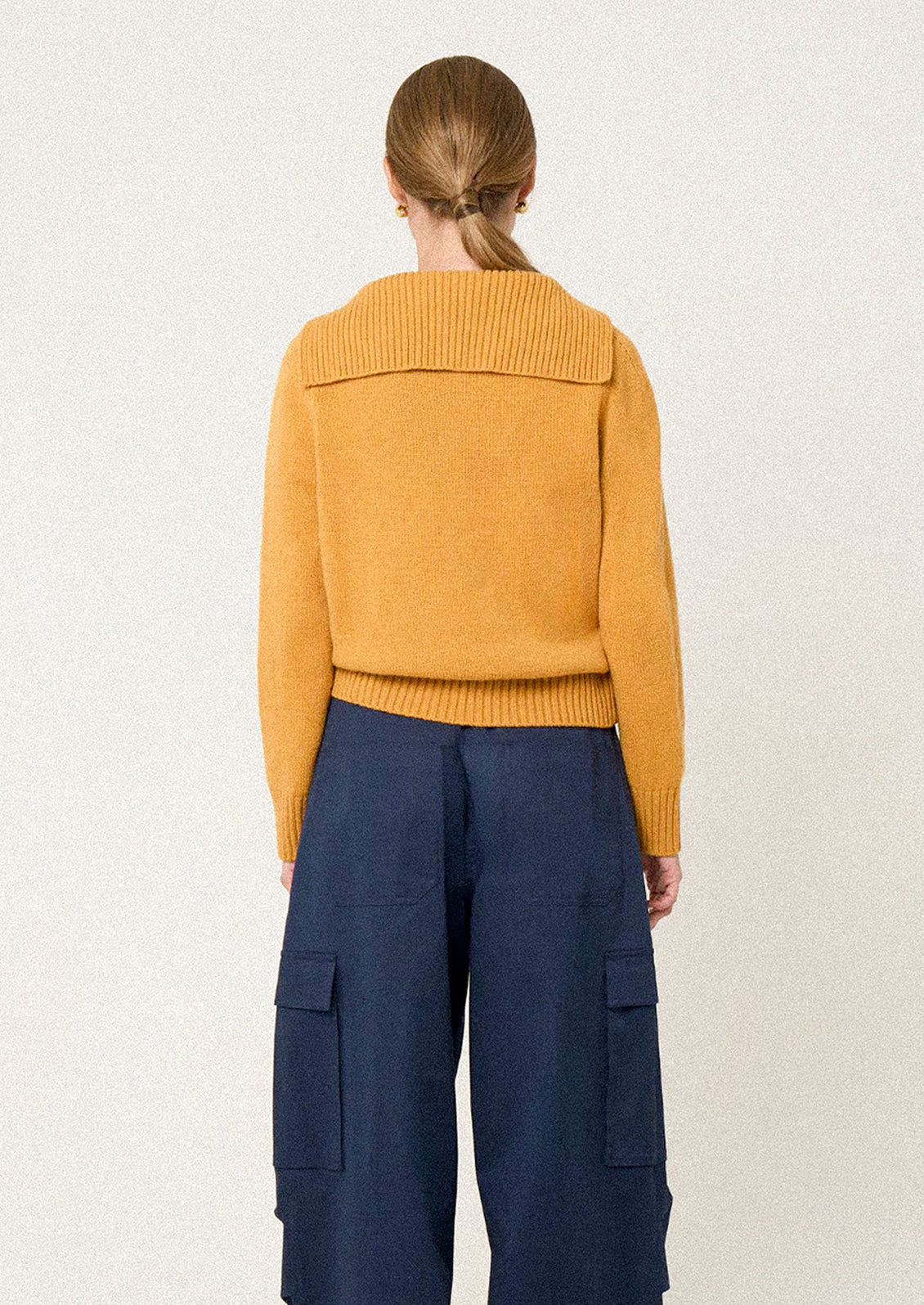 Person wearing a mustard yellow sweater and blue pants on a light background