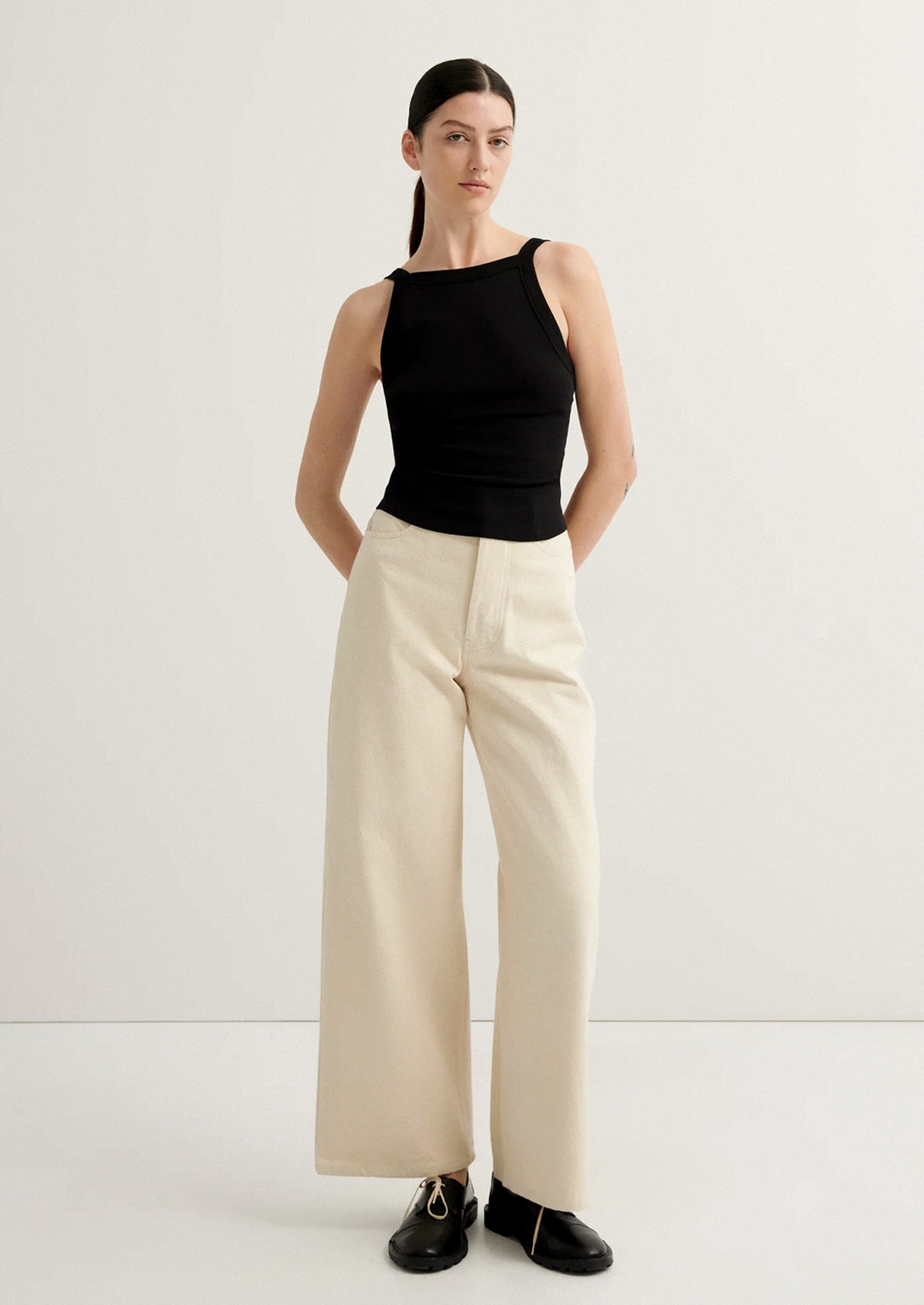 Woman wearing a black sleeveless top and beige wide-leg pants on a white background