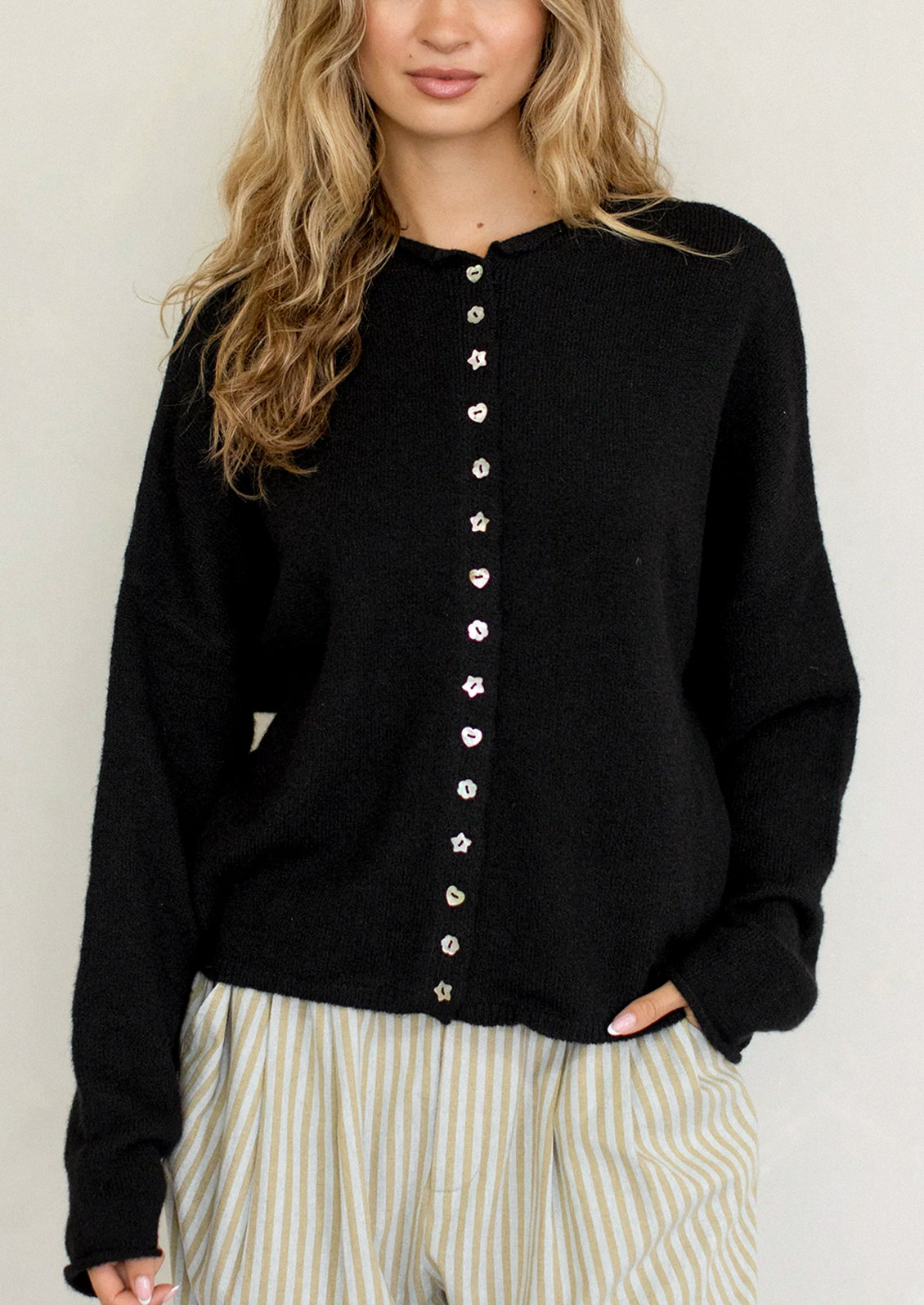 Person wearing a black cardigan with button details against a plain background