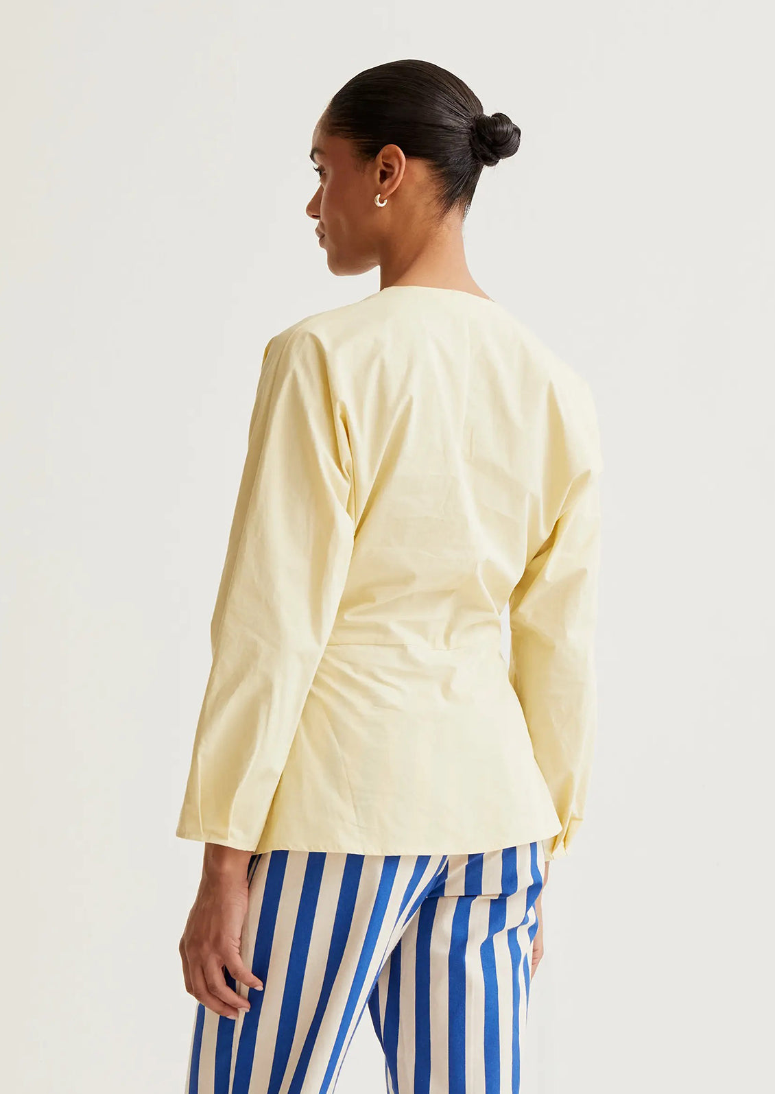 Woman wearing a light yellow top and blue striped pants on a white background