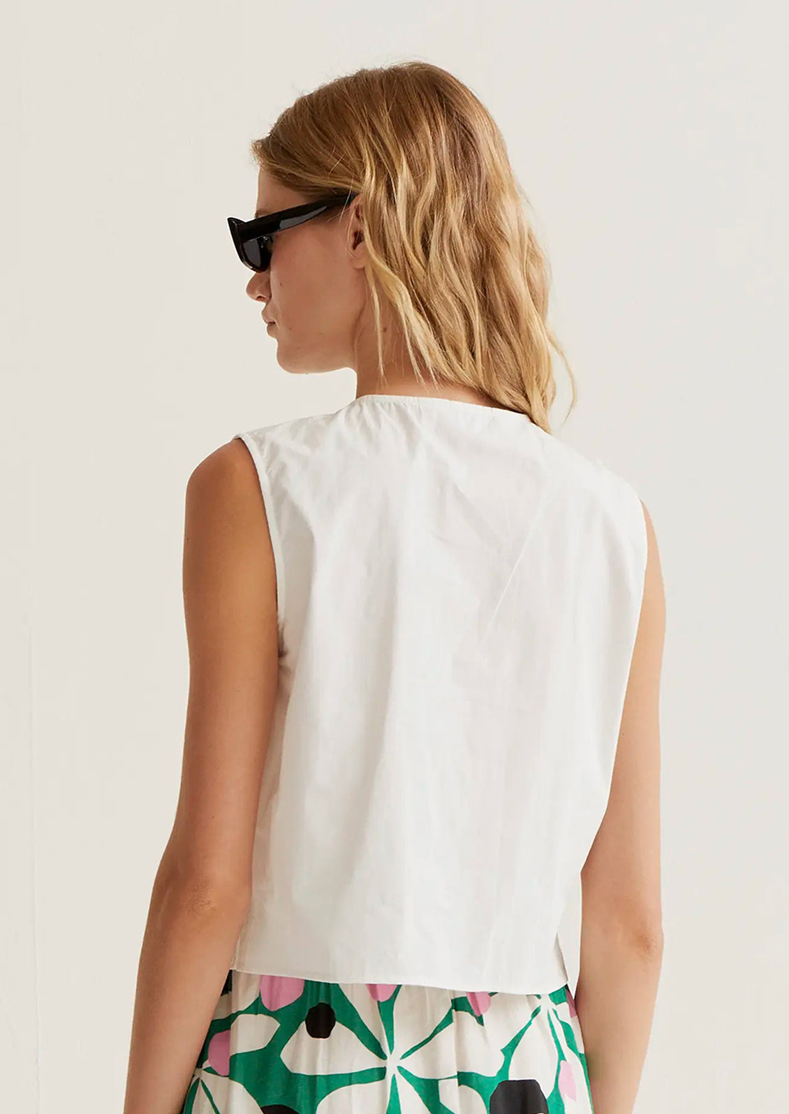 Woman wearing a white sleeveless top and colorful pants on a plain background