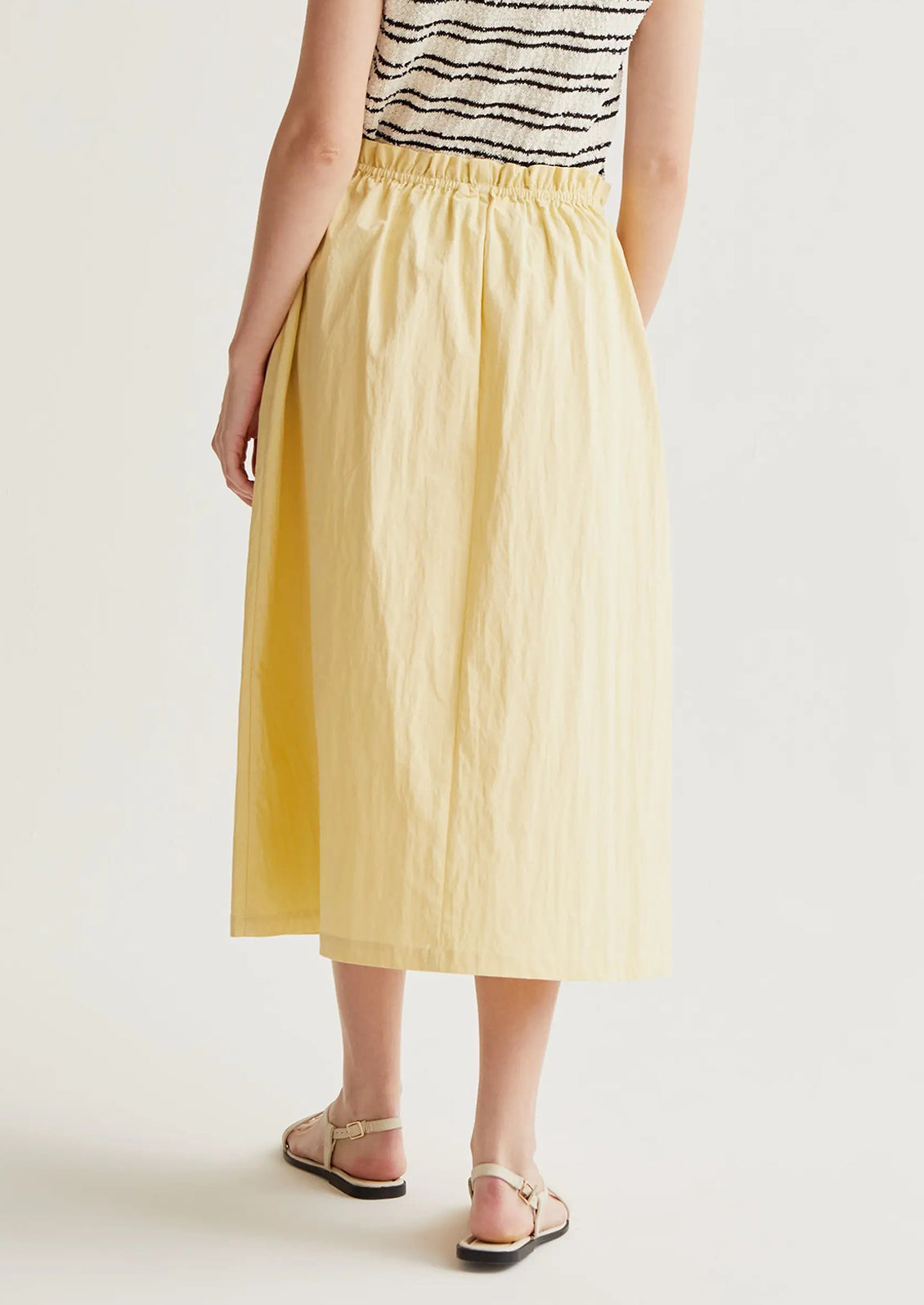 Person wearing a yellow skirt and black and white striped top on a plain background