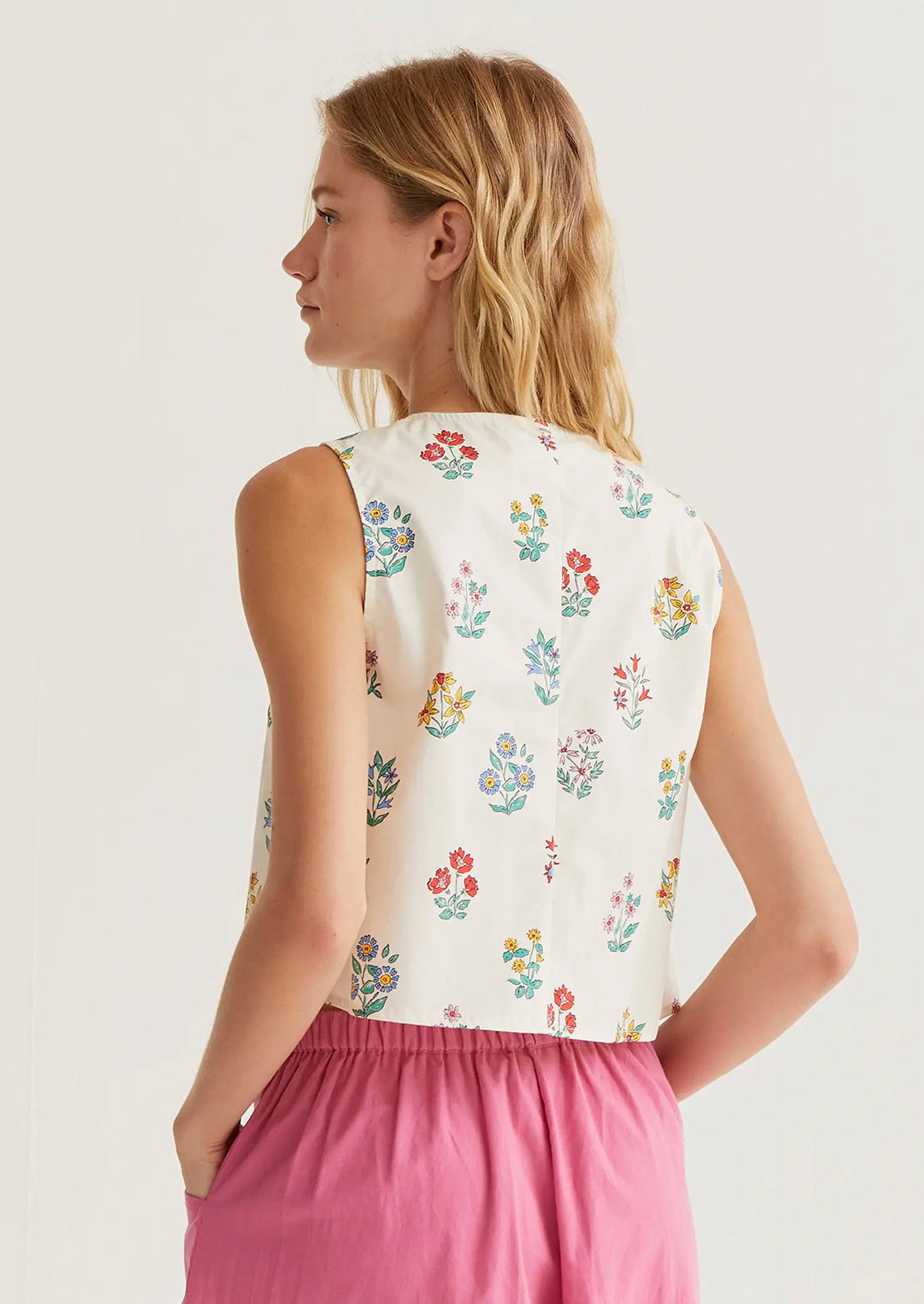 Woman wearing a sleeveless floral top and pink pants on a plain background