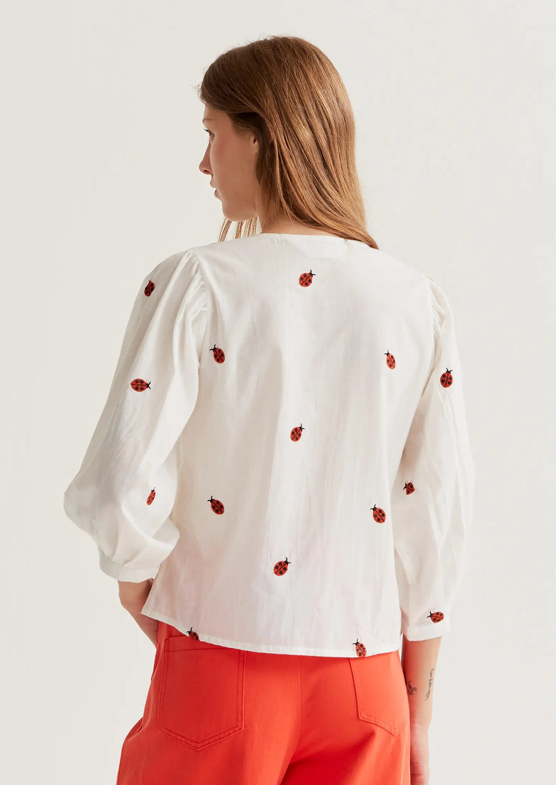 Woman wearing a white blouse with red floral patterns on a plain background