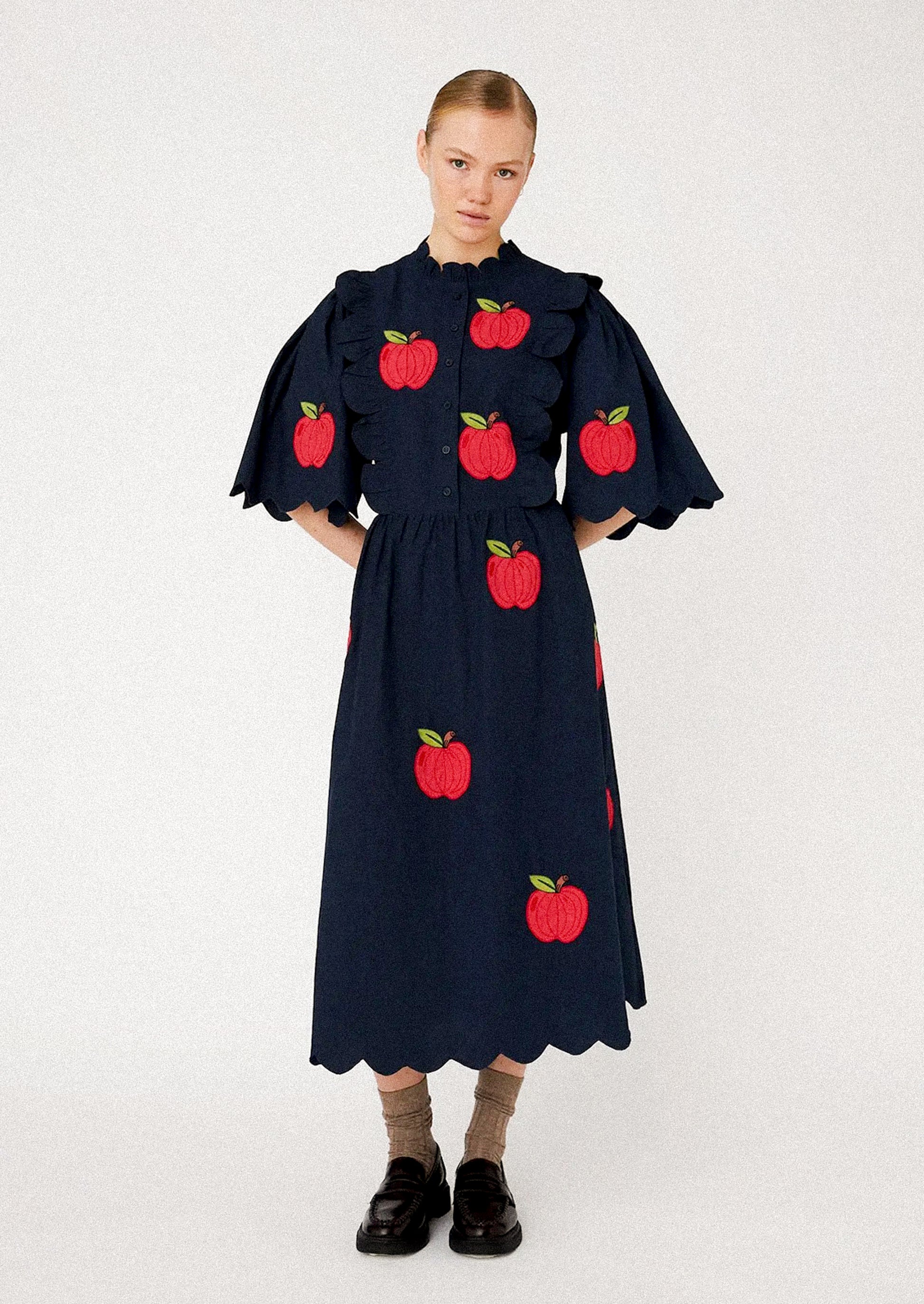 Woman wearing a navy dress with red apple patterns.
