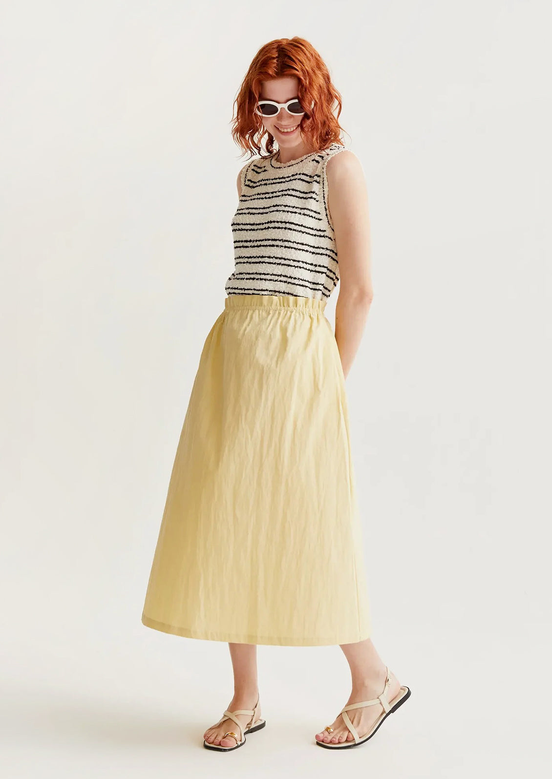 Woman wearing a striped sleeveless top and yellow skirt on a white background