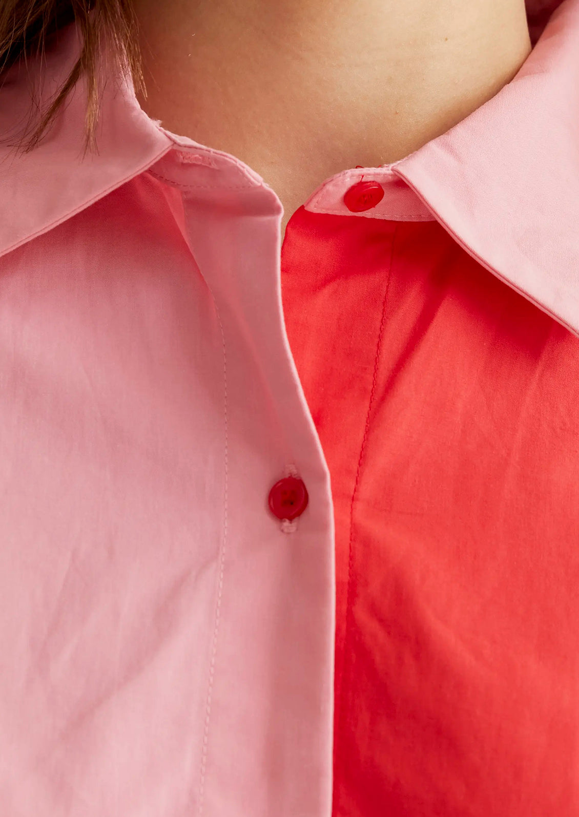 Close-up of a person wearing a pink shirt with a red button.