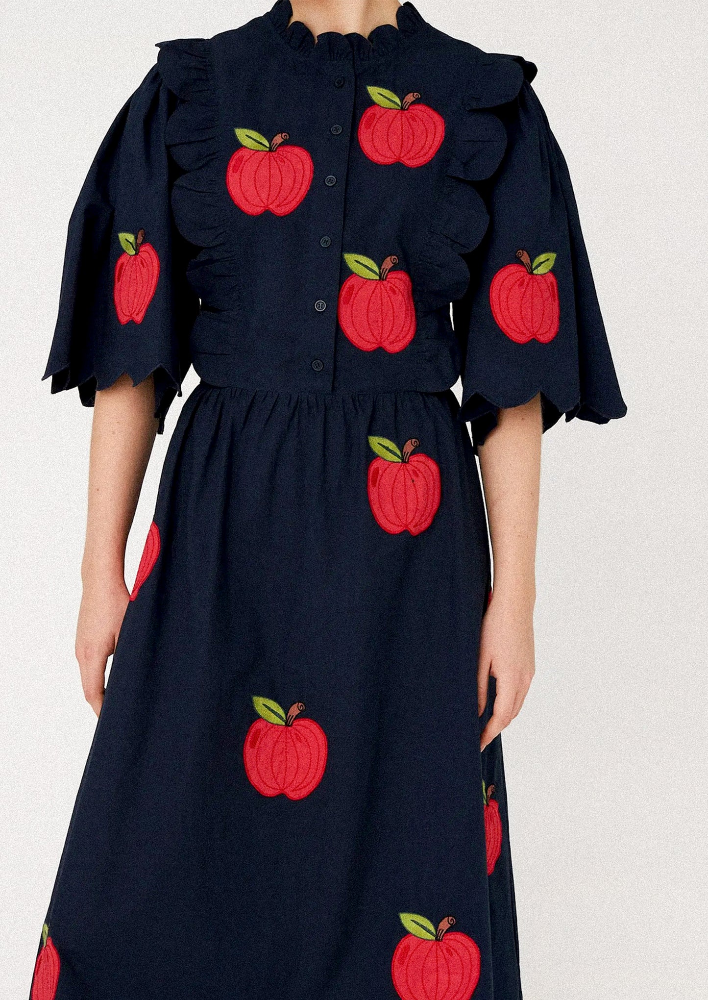 Woman wearing a navy dress with red apple patterns.