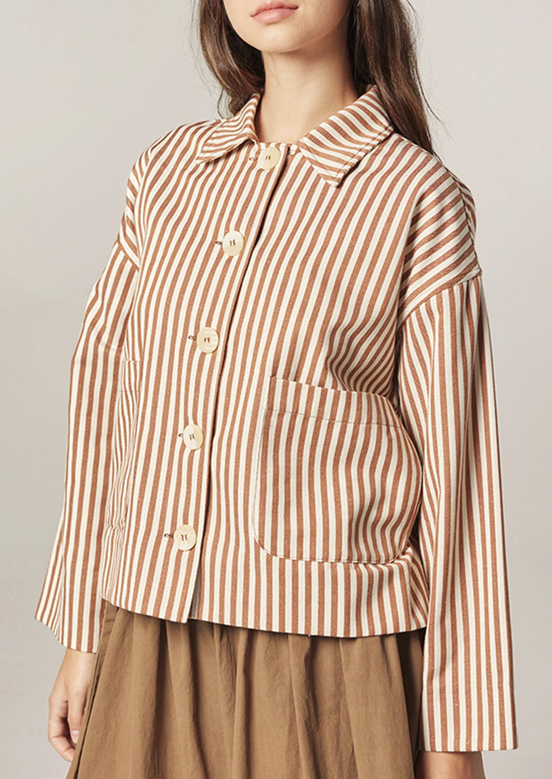 Woman wearing a brown and white striped shirt with a neutral background