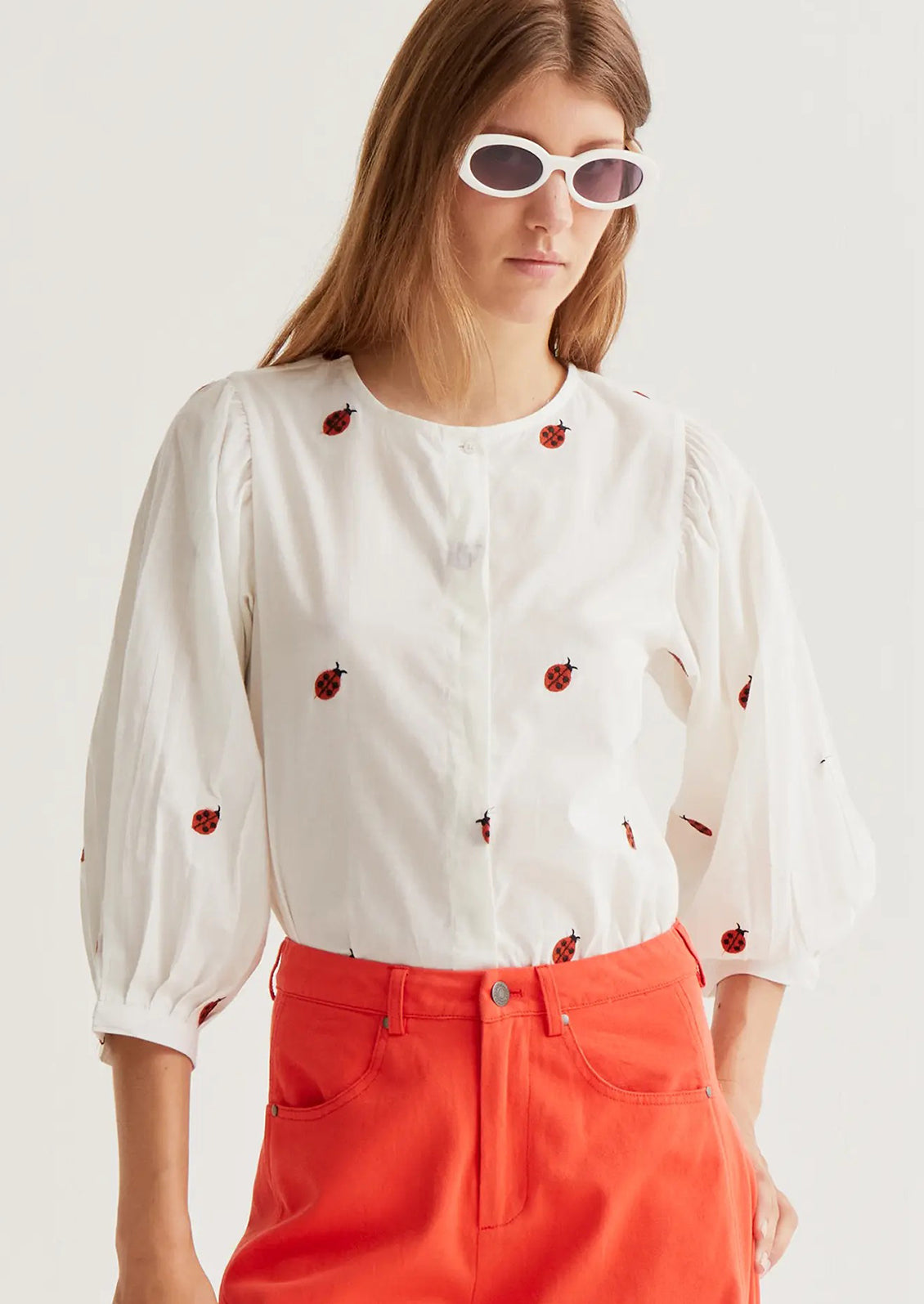Woman wearing a white blouse with red patterns and red pants on a light background
