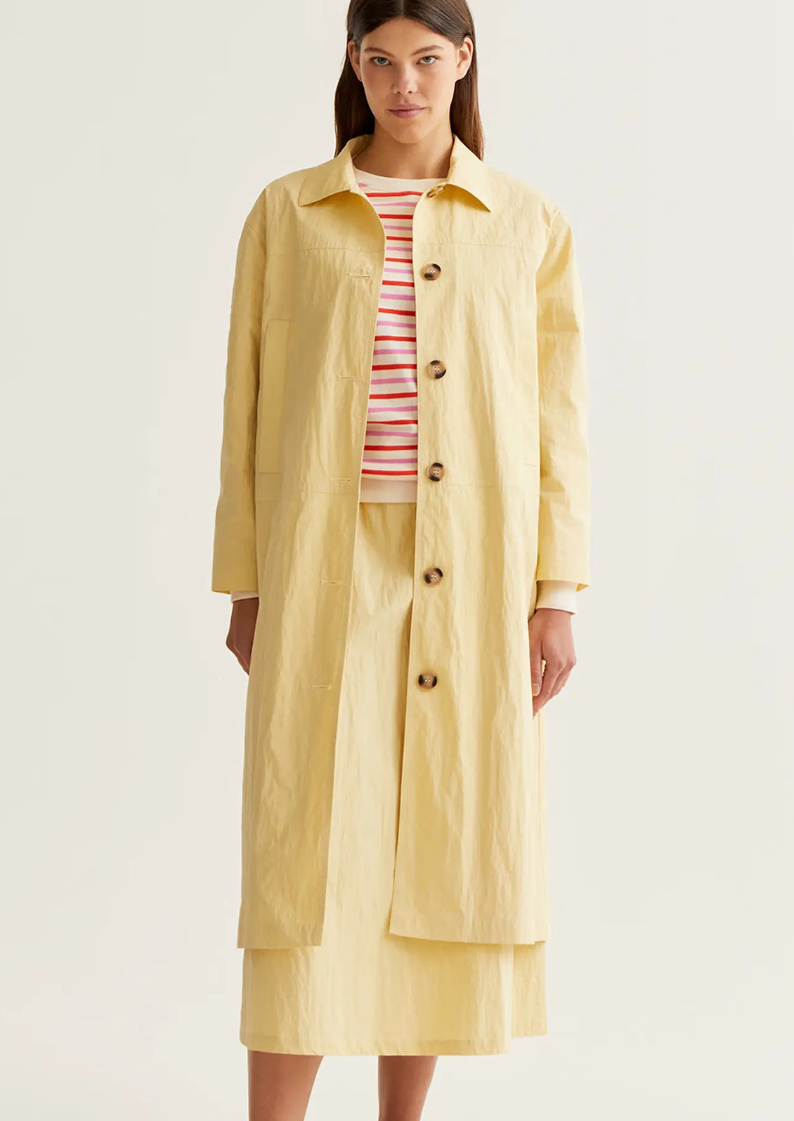 Woman wearing a yellow raincoat over a striped shirt on a white background