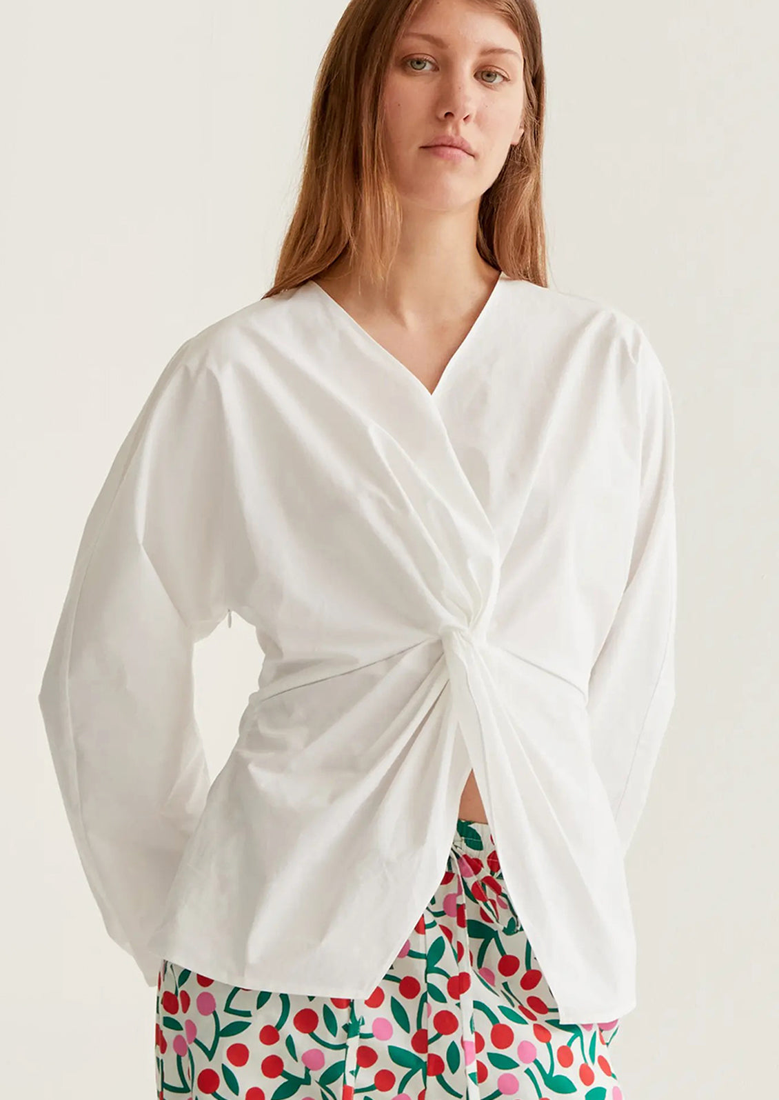 Woman wearing a white wrap top with floral pants on a plain background