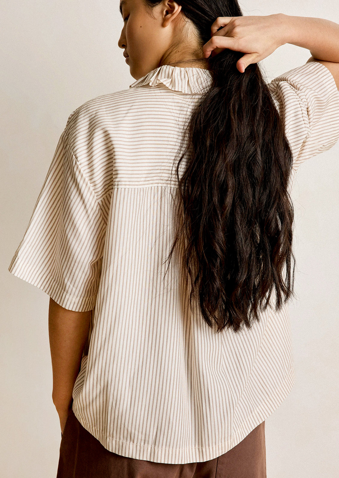 Person wearing a light-colored striped shirt with a neutral background