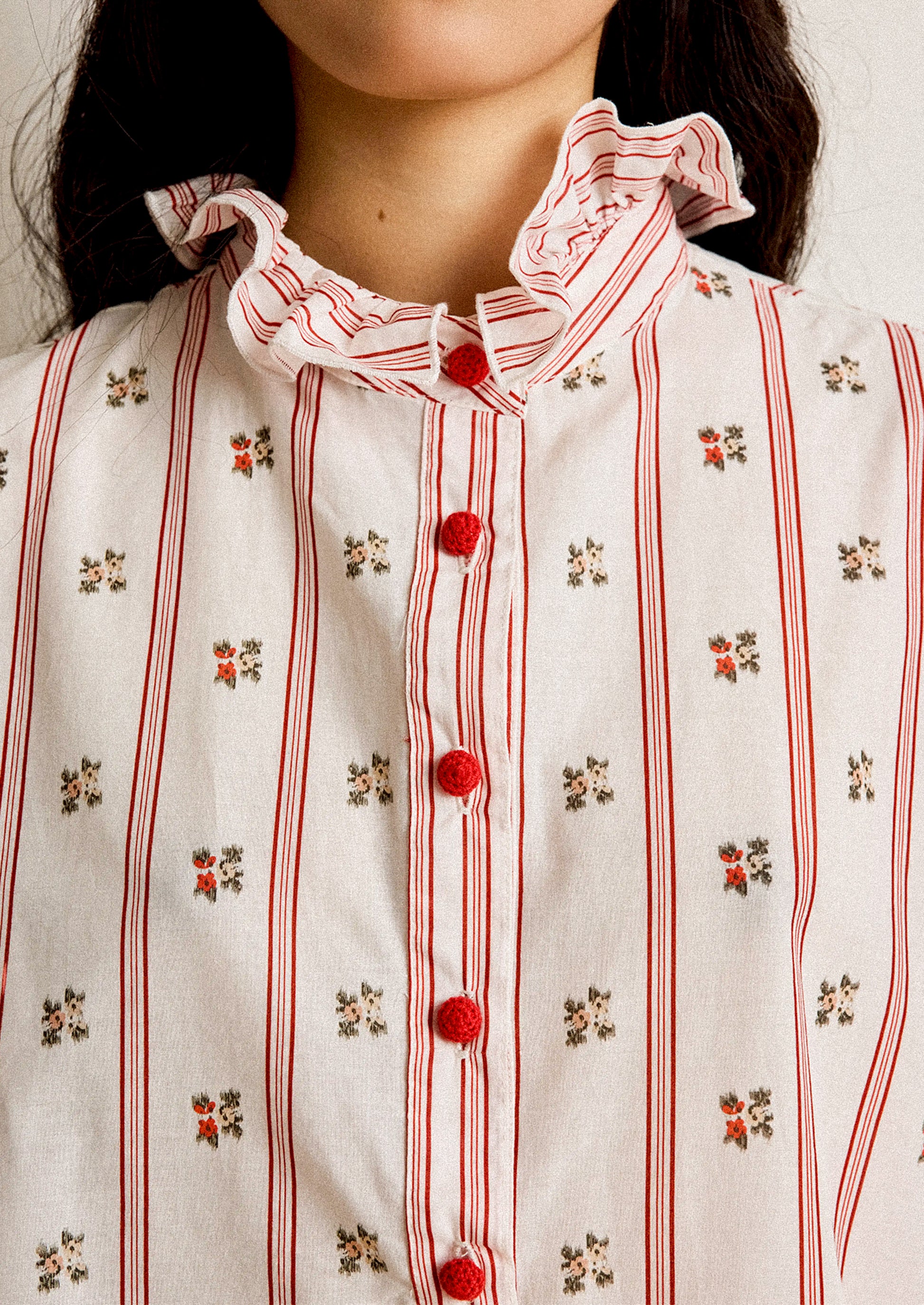 Close-up of a person wearing a white blouse with red stripes and floral patterns, featuring red buttons.
