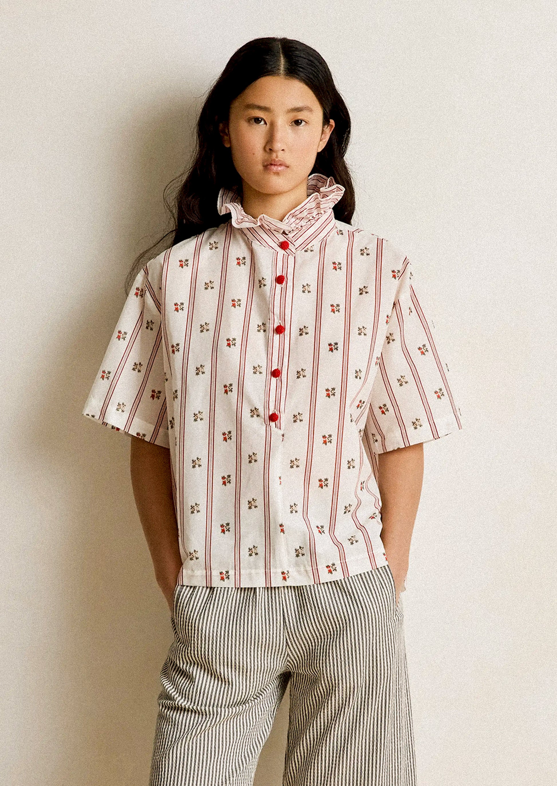 Person wearing a patterned shirt with red buttons against a plain background