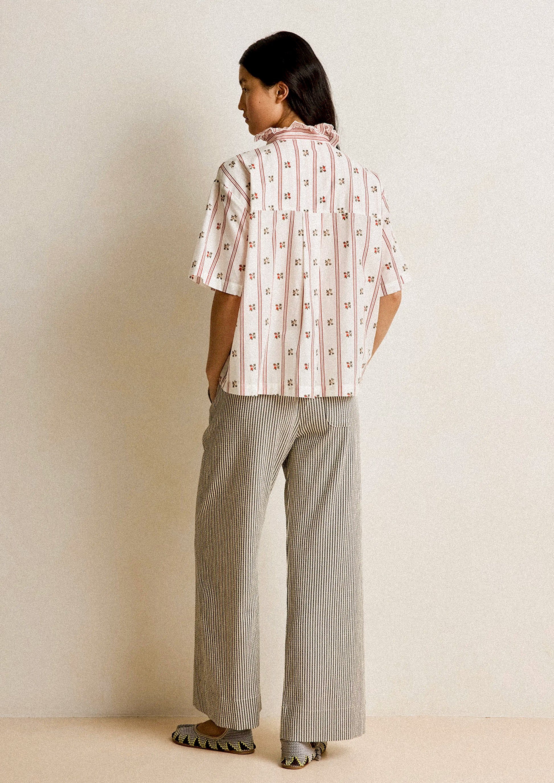 Person wearing a patterned shirt and striped pants against a plain background