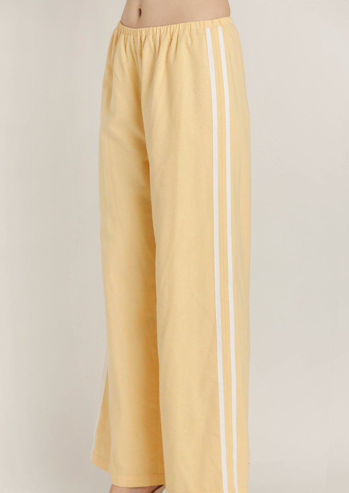 Yellow wide-leg pants with two vertical white stripes down the side, shown on a model cropped from the waist down against a plain light background.