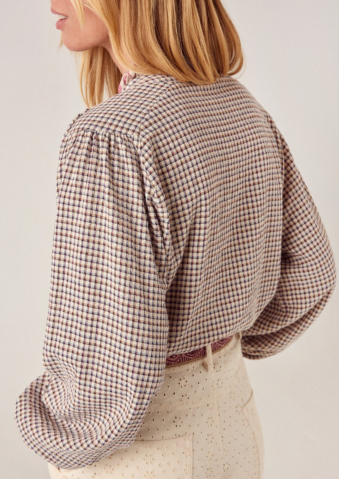 A person wearing a long sleeve blouse in brown check.