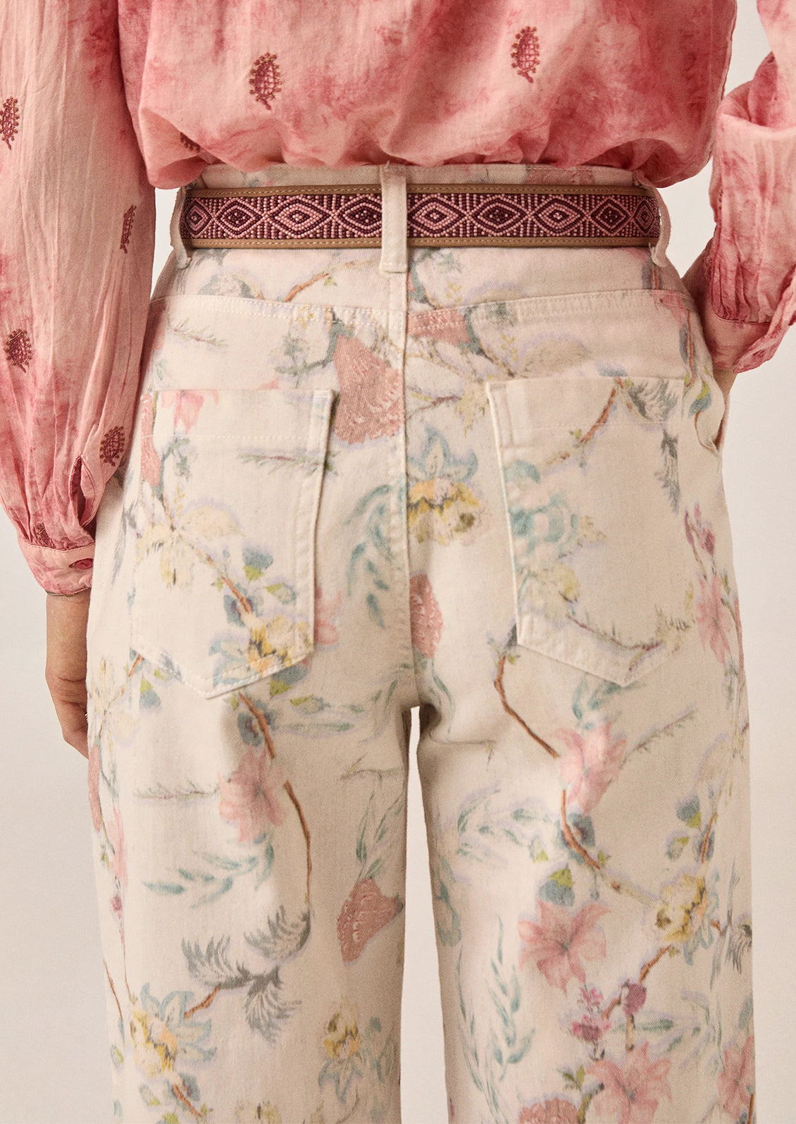 A person wearing a pair of white denim pants with pastel floral print.