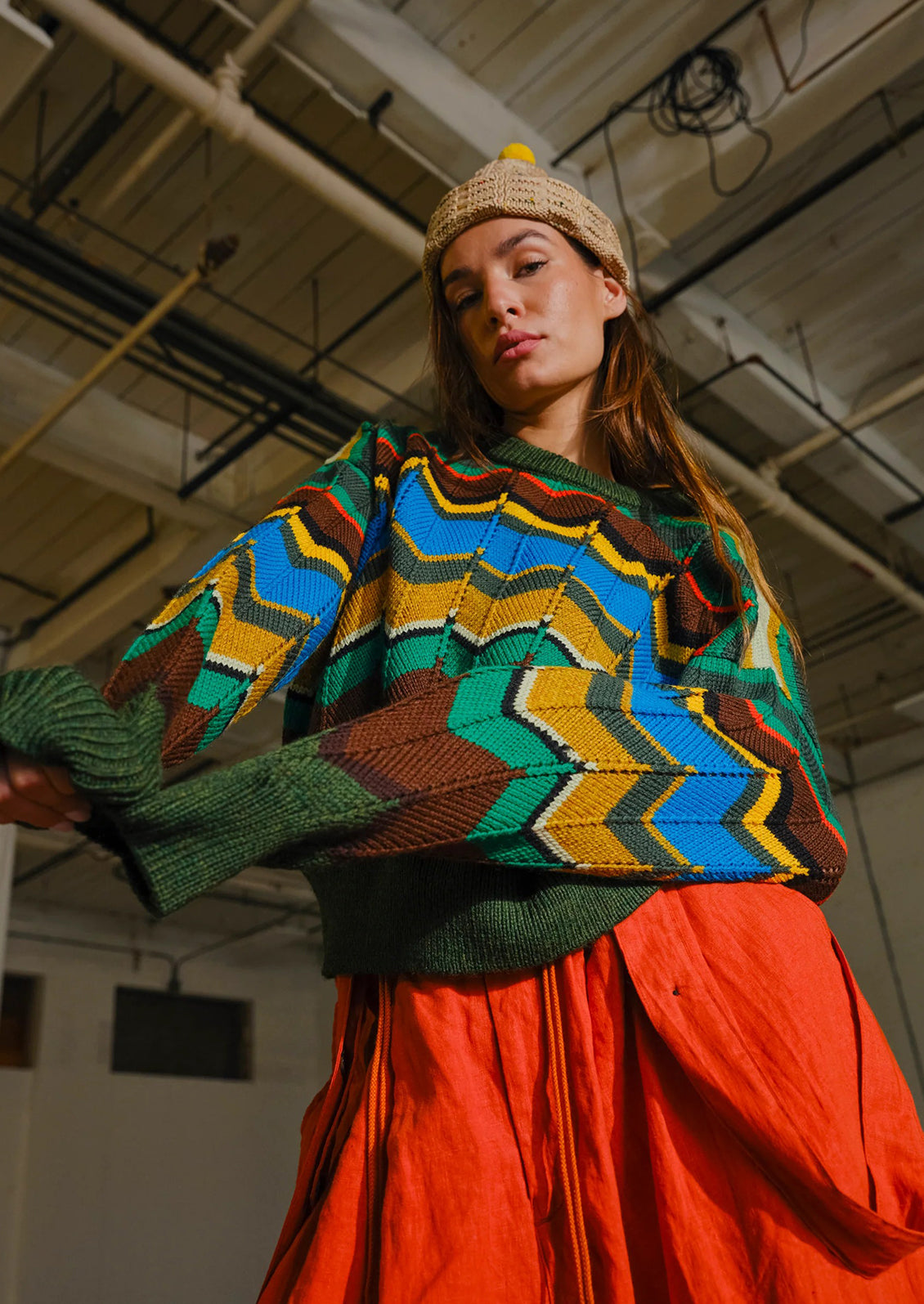 Person wearing a colorful patterned sweater and red skirt in an indoor setting