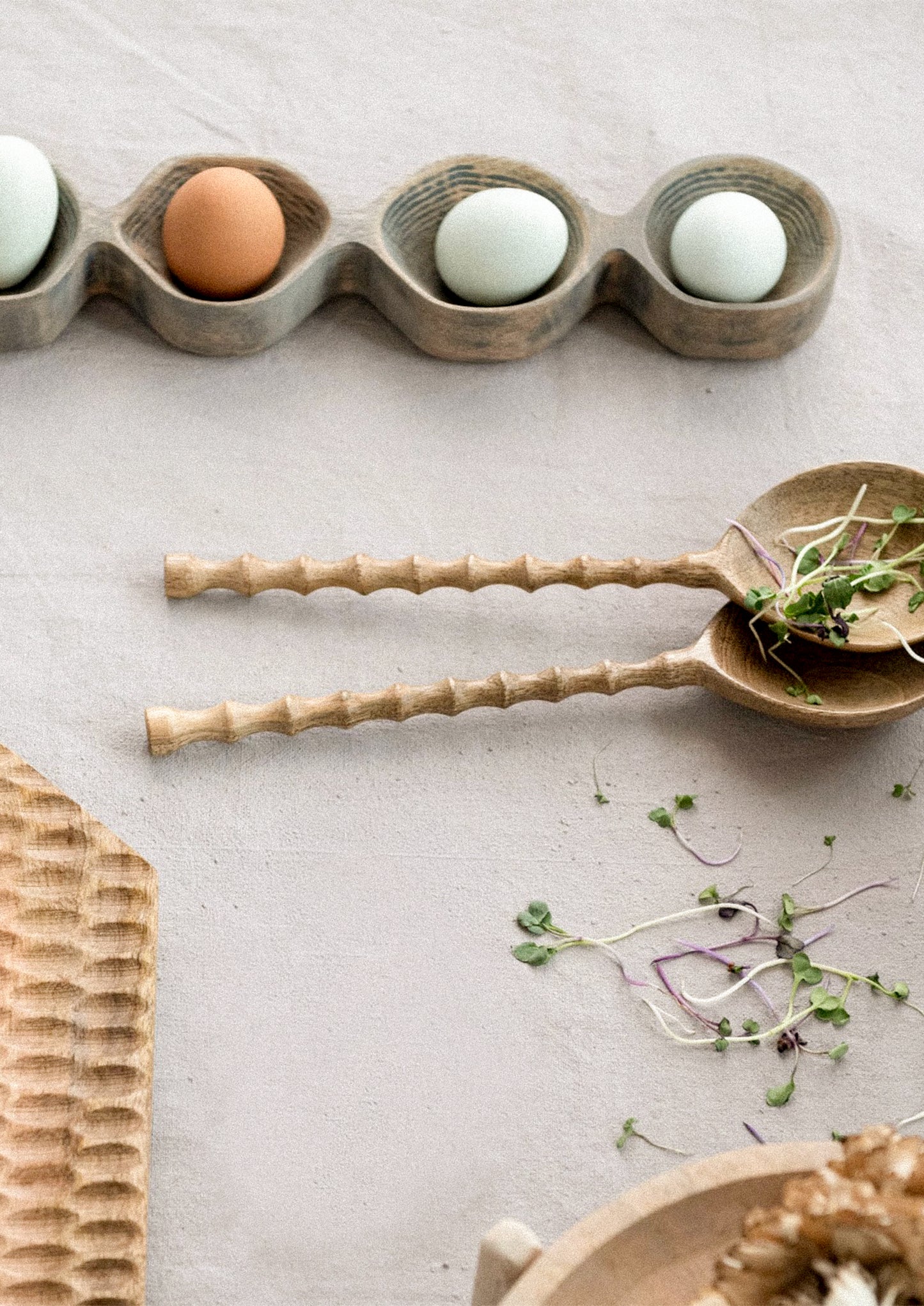 Wooden egg holder with eggs on a light surface, accompanied by a wooden spoon with sprouts.