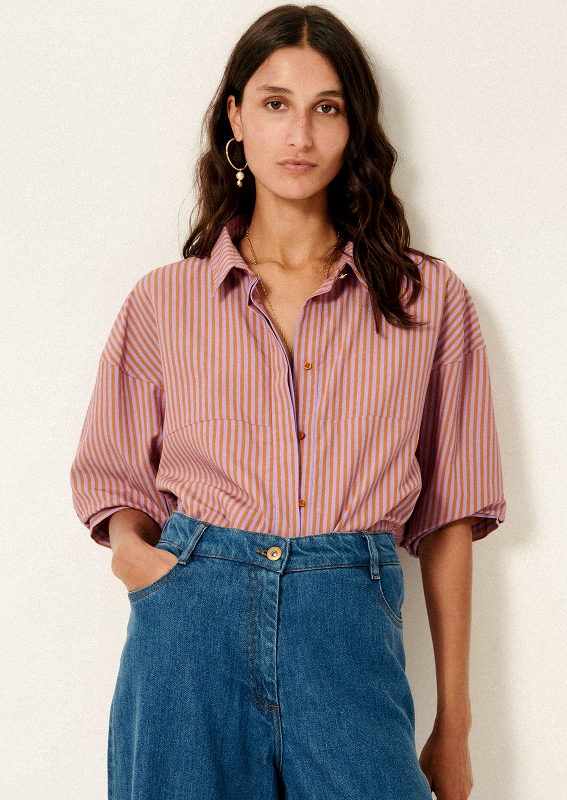 A woman wearing a short collared shirt in orange and purple stripes.
