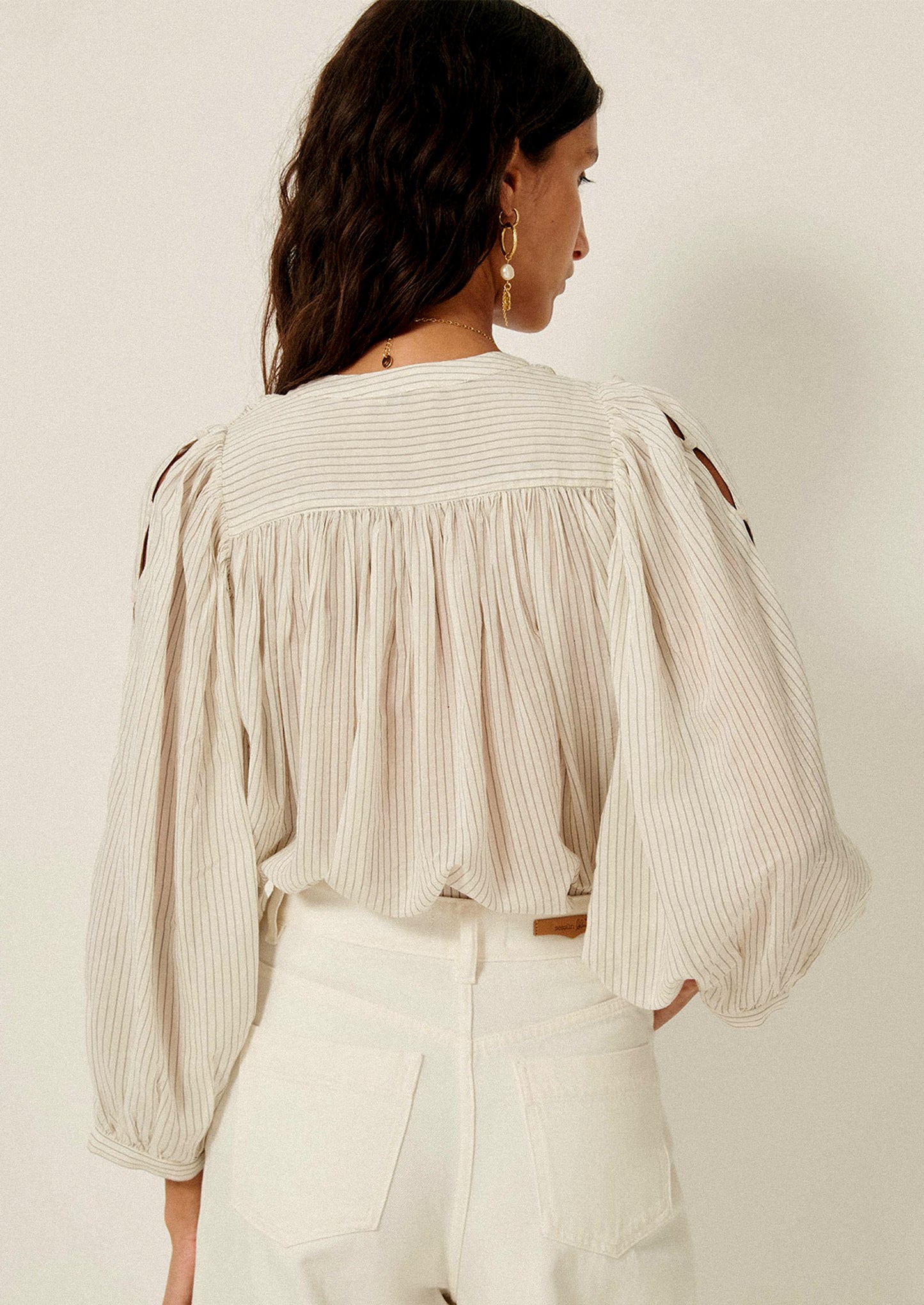 A woman wearing a white blouse with black pinstripe pattern, and cutout detailing on sleeves.