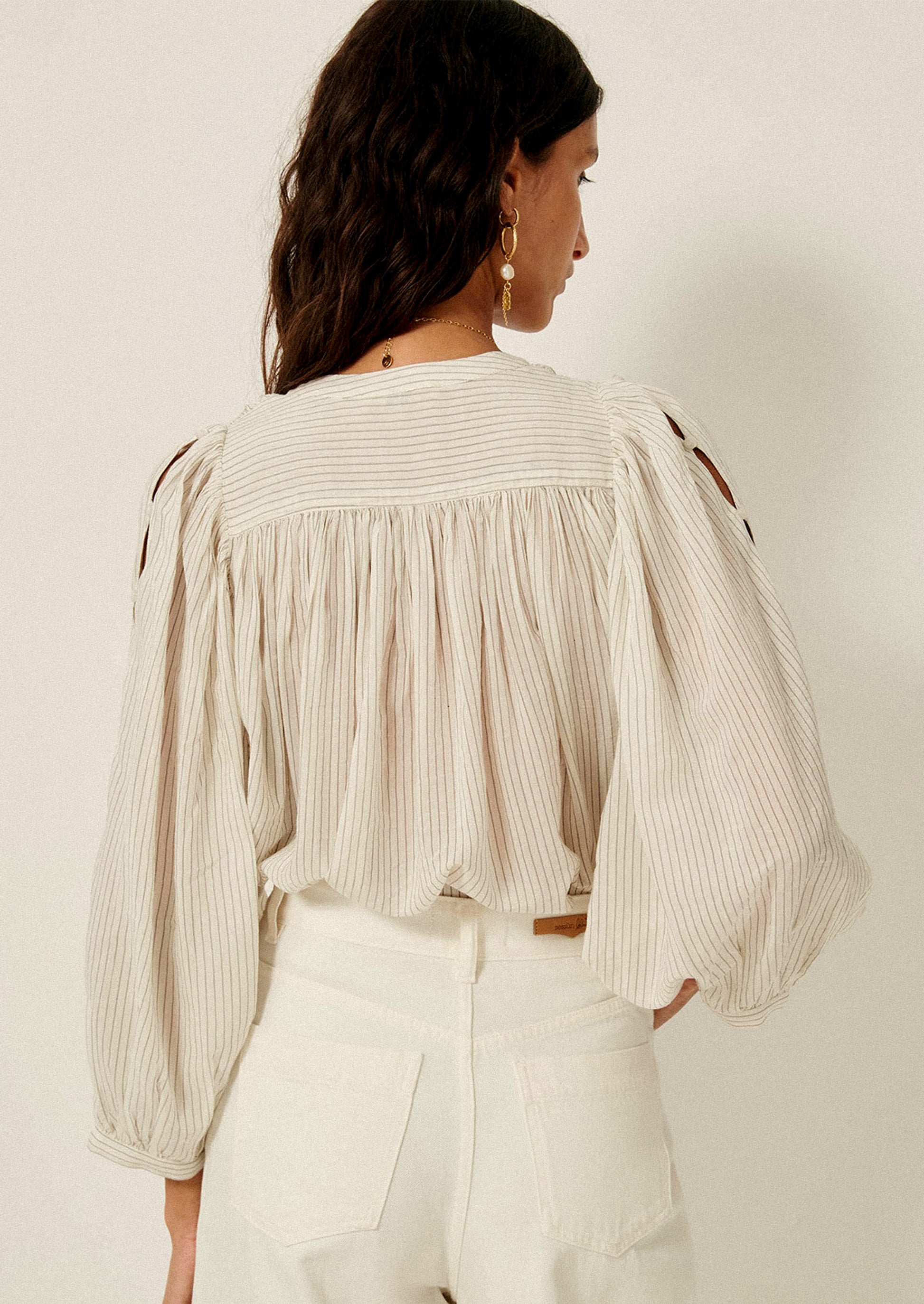 A woman wearing a white blouse with black pinstripe pattern, and cutout detailing on sleeves.