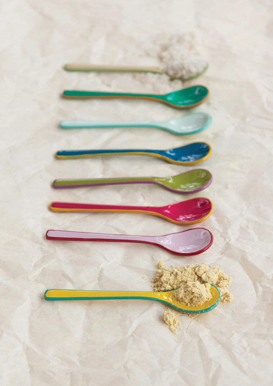 Colorful spoons arranged on a textured surface with a small amount of powder.