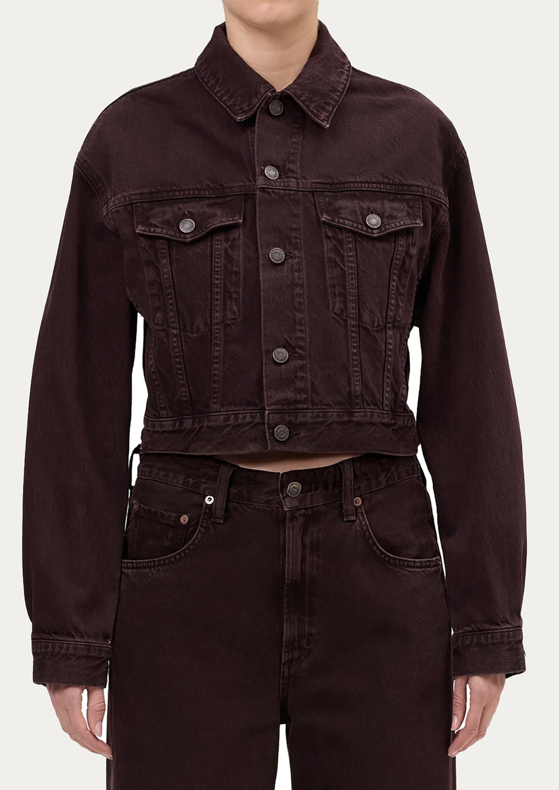 Person wearing a dark brown denim jacket and pants on a white background