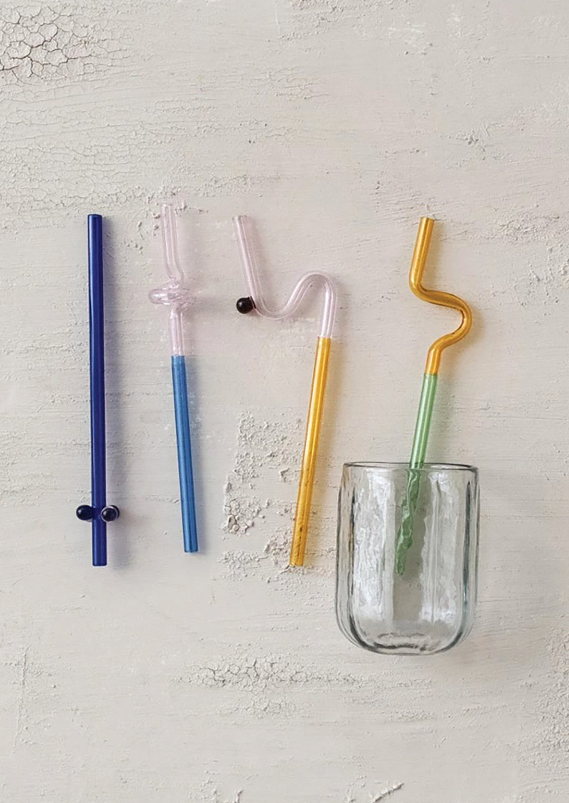 Set of four colorful straws with a glass on a light gray background